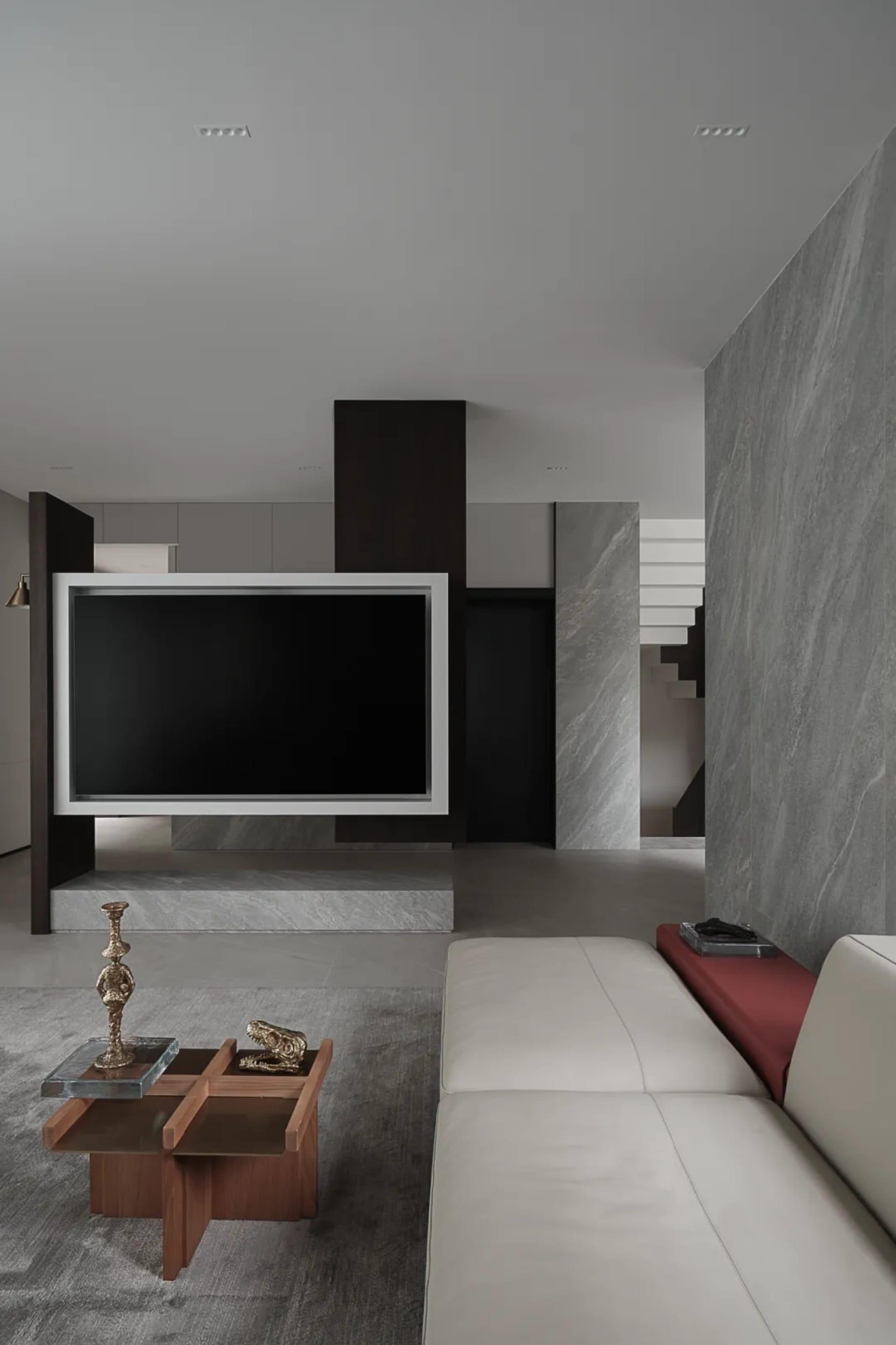 A modern living room with a white leather sofa, a marble coffee table, and a large television screen mounted on a marble colu