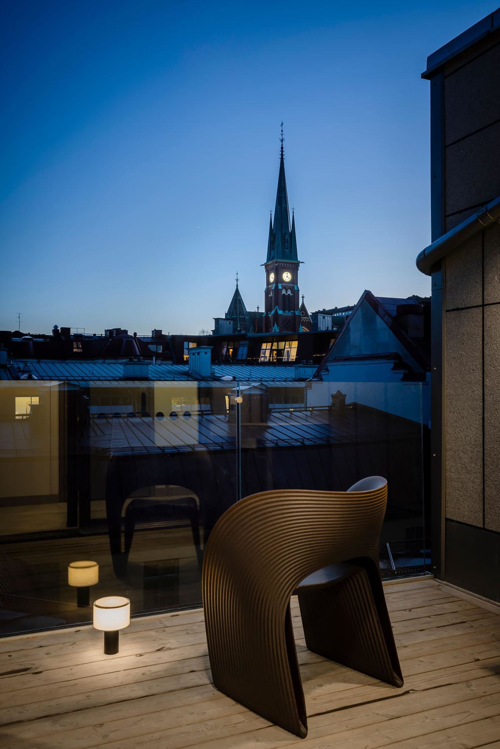 Wooden chair on a deck overlooking a city skyline at dusk, featuring a tall clock tower.
