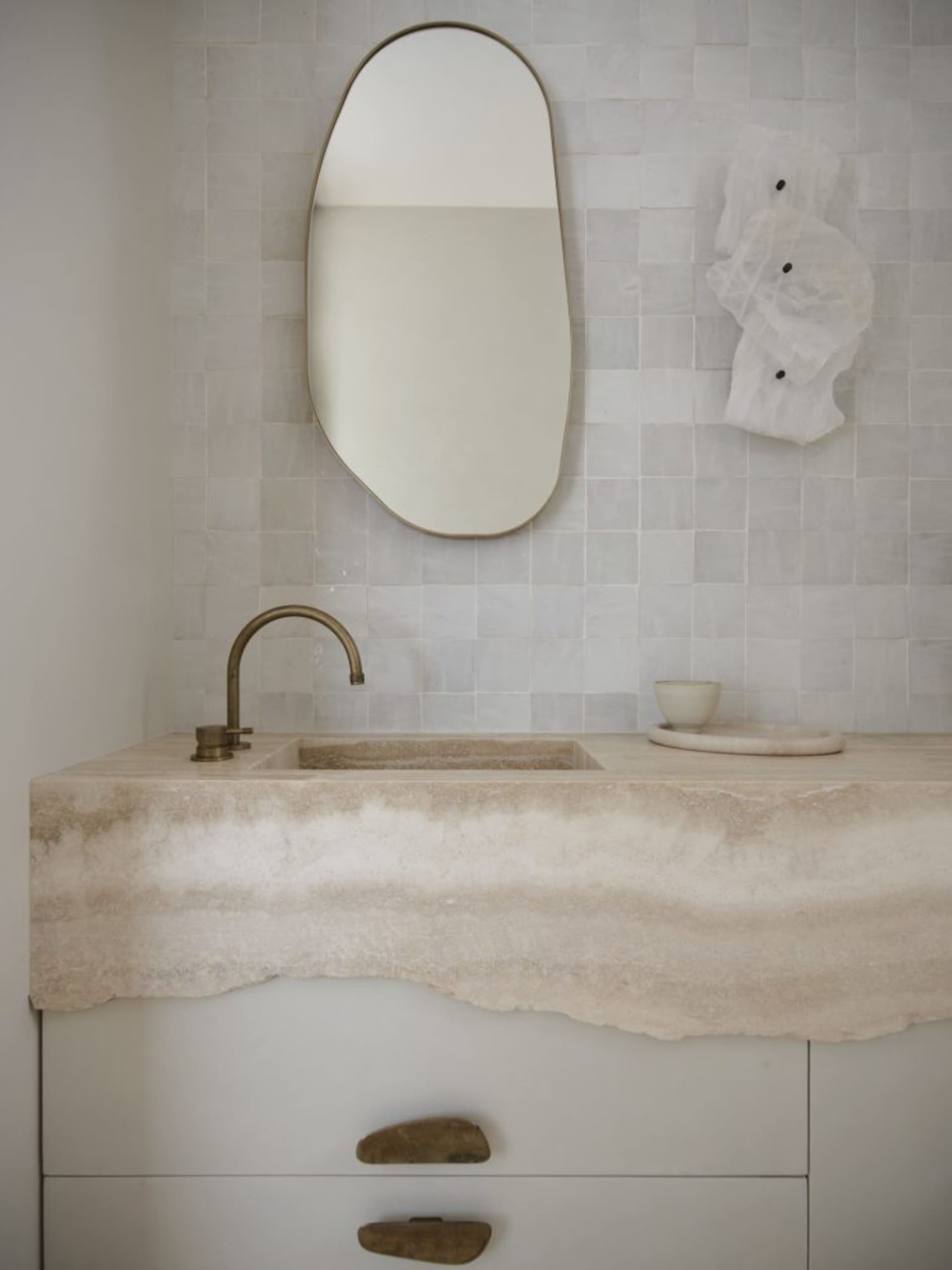 A modern bathroom with a natural stone sink, an oval-shaped mirror, and a small decorative bowl placed on a stone countertop.