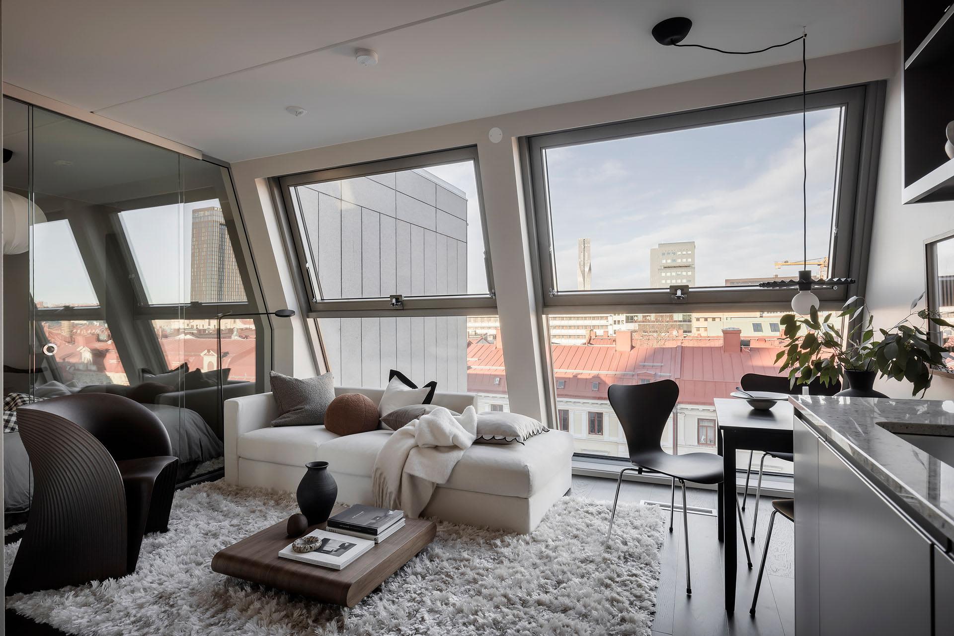 A modern living room with large glass windows, white furniture, and minimalist decor.