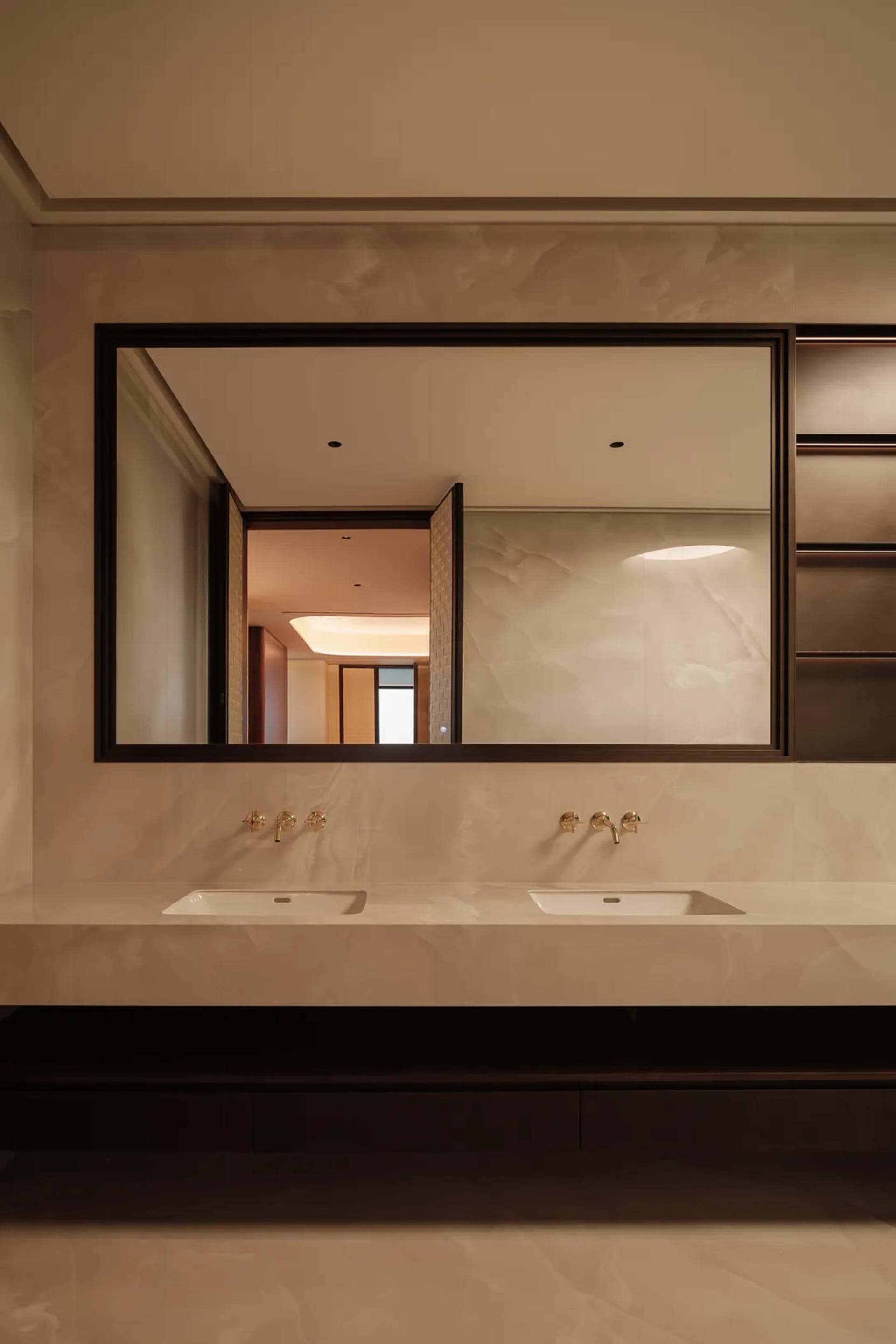 Modern bathroom with marble countertops and sinks, dual faucets, and a large mirror.