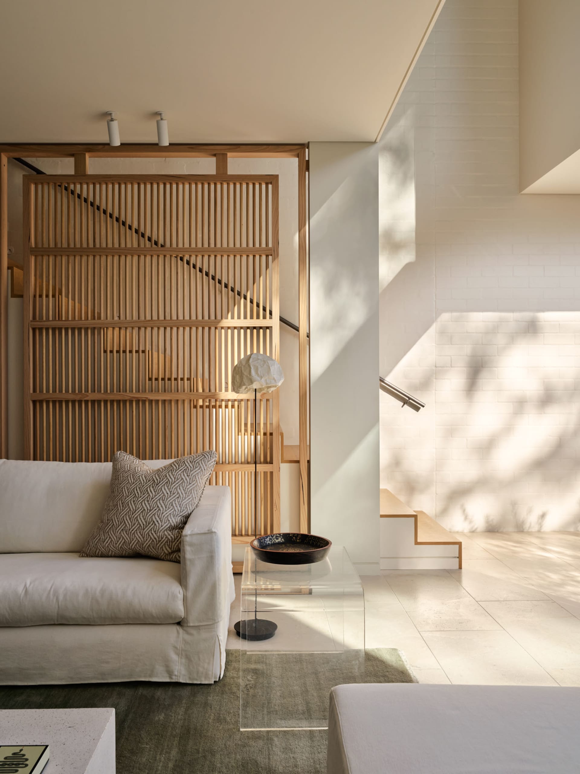 Minimalist living room featuring a wood-paneled wall and a white sofa with a patterned pillow.