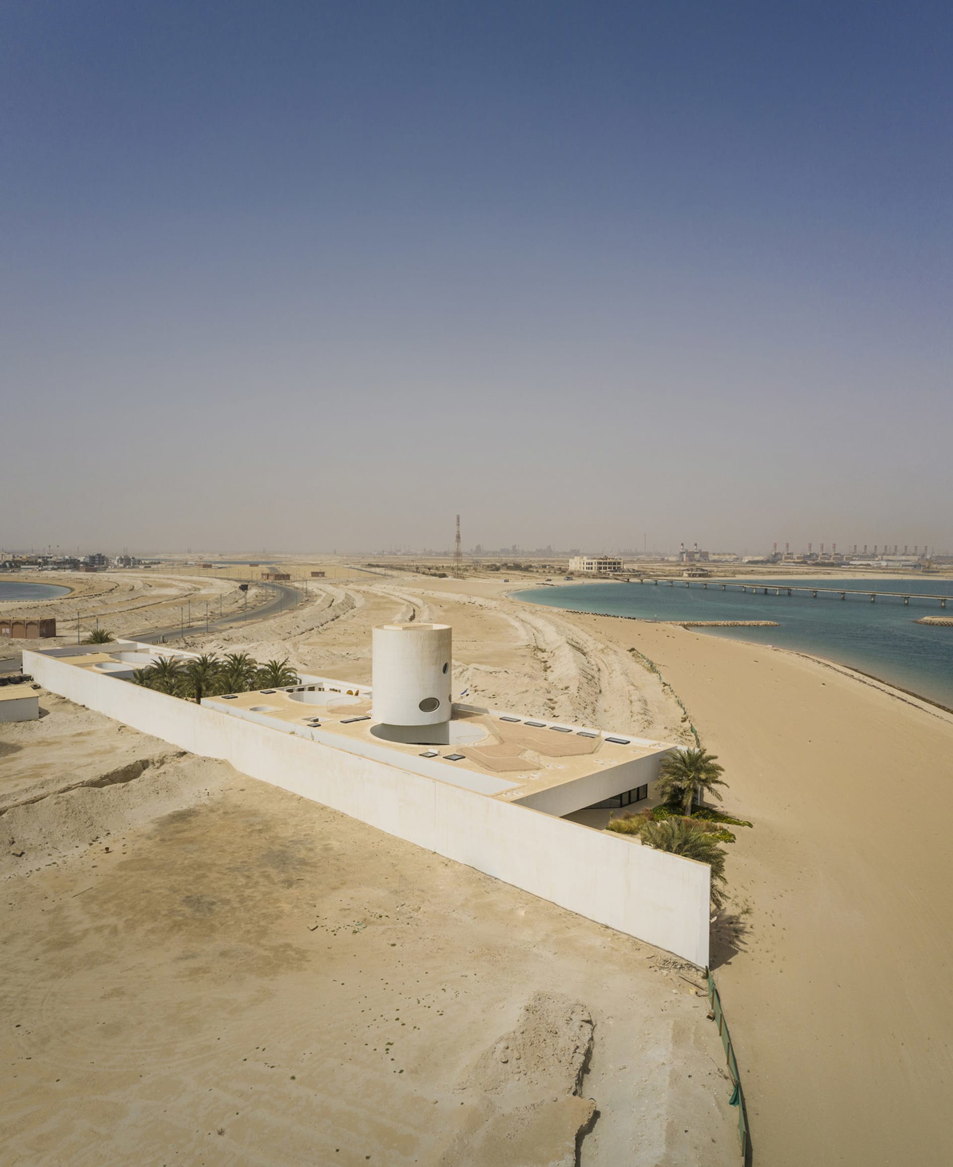 Modern beach-front property with a cylindrical concrete structure on a sandy beach.