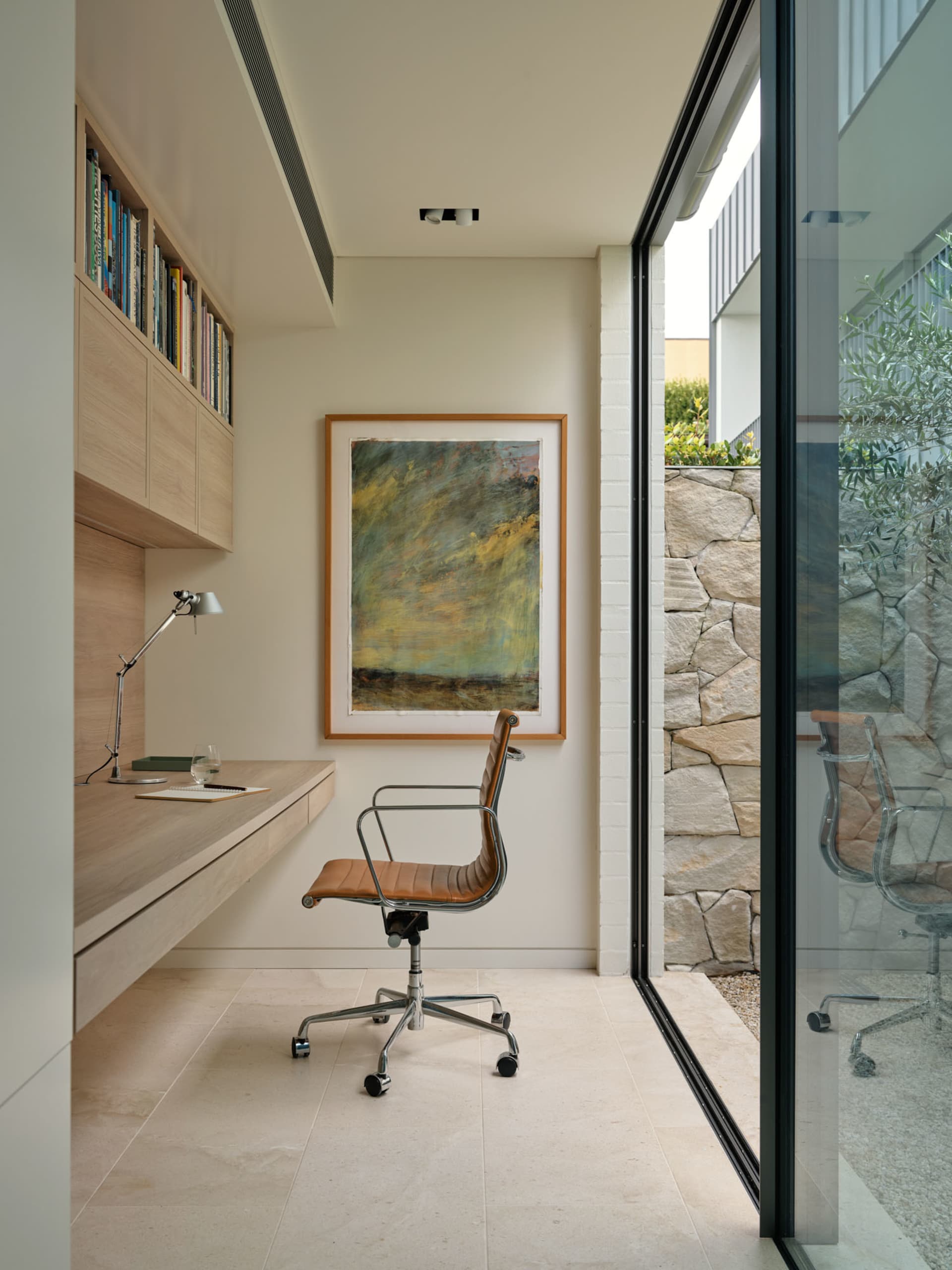 A modern office space featuring a wooden desk, glass window, and abstract painting.