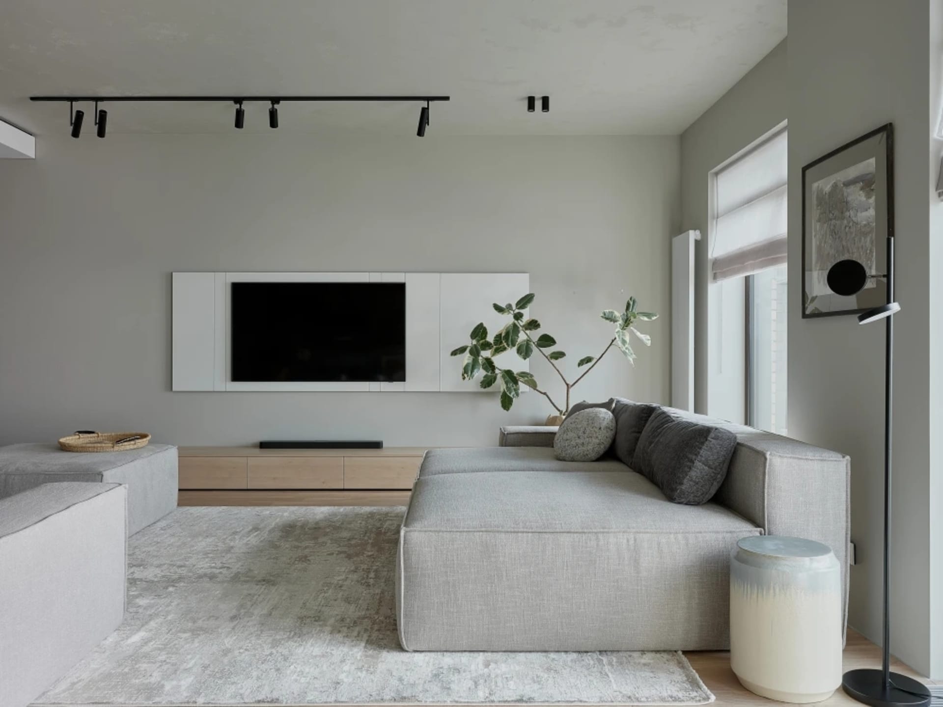 Modern minimalist living room with light grey fabric furniture, large windows, and a sleek entertainment console.