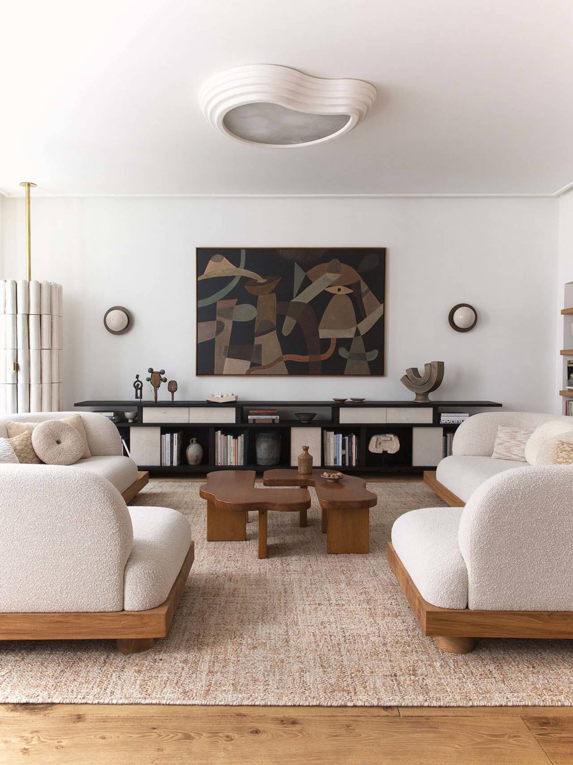 A minimalistic living room with beige wool sofas and wooden accents, featuring abstract art and a low-profile coffee table on