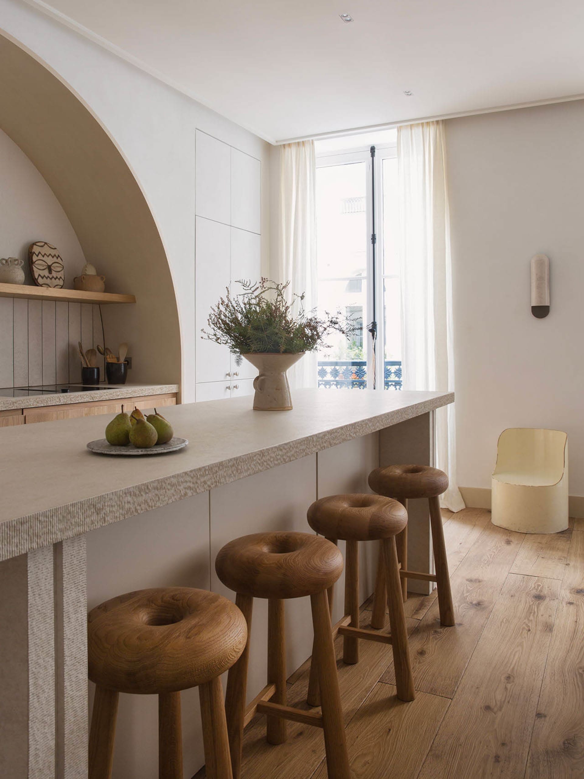 A modern residential kitchen featuring minimalist design with wooden stools and countertops.