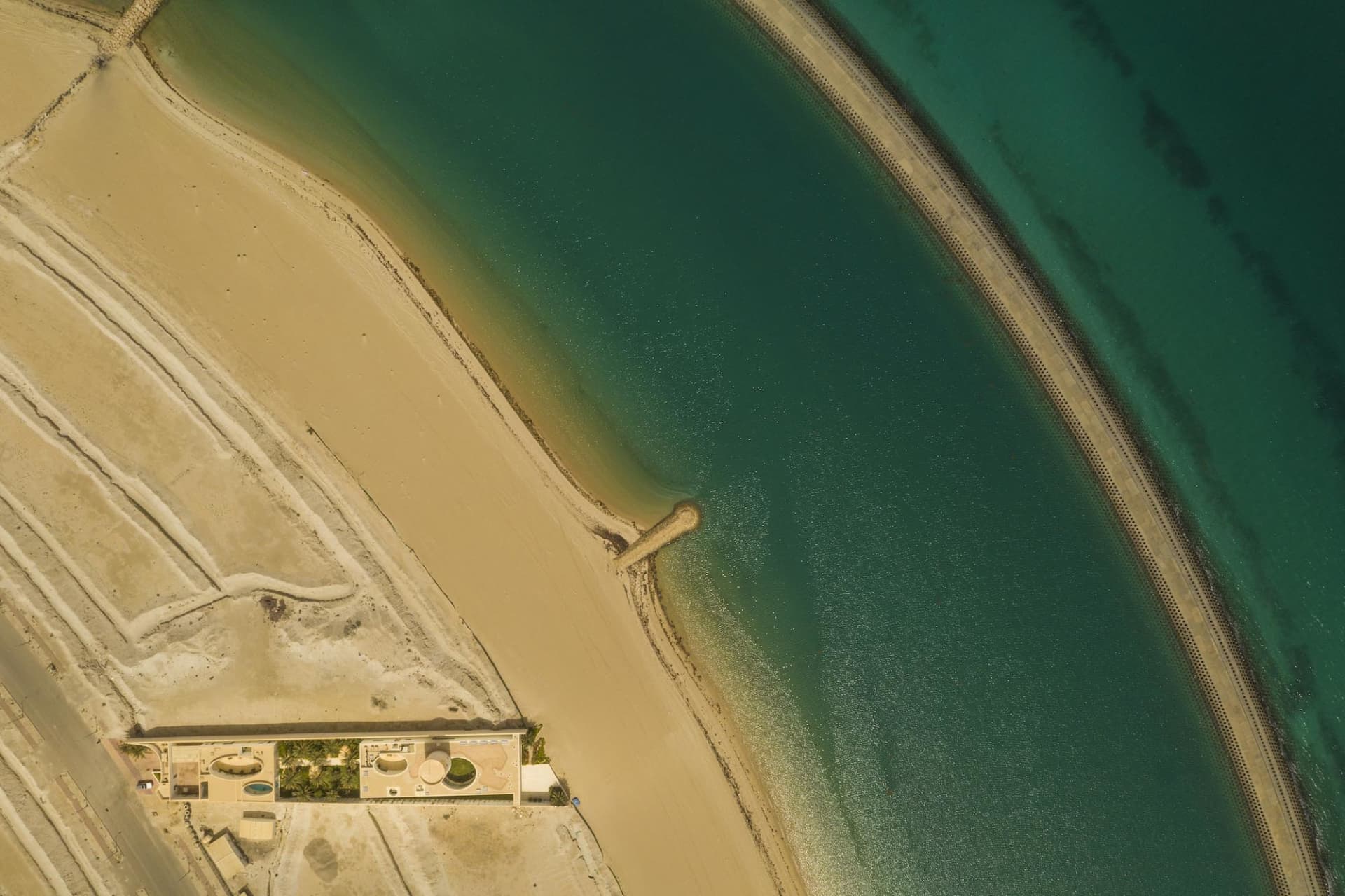 Aerial view of a modern beachfront property with concrete structures and sandy beach.