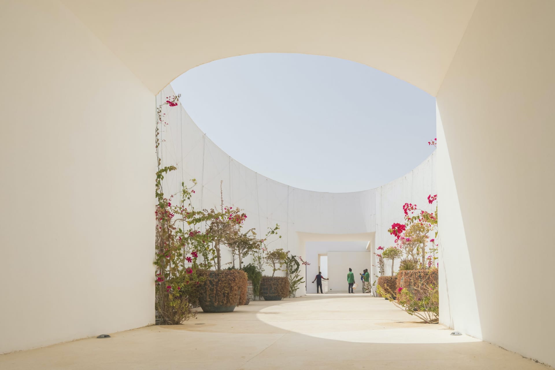 A modern white concrete interior with open archways and plants.