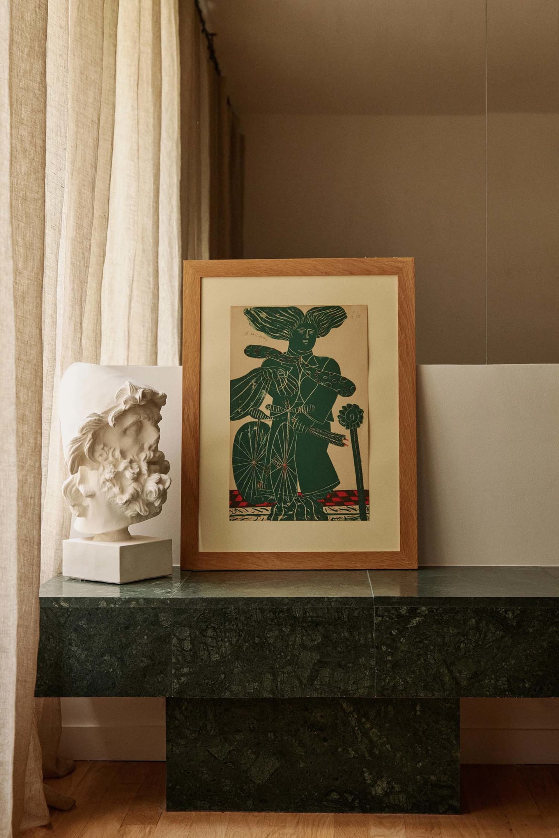 A framed artwork and a marble bust displayed on a green marble console table.
