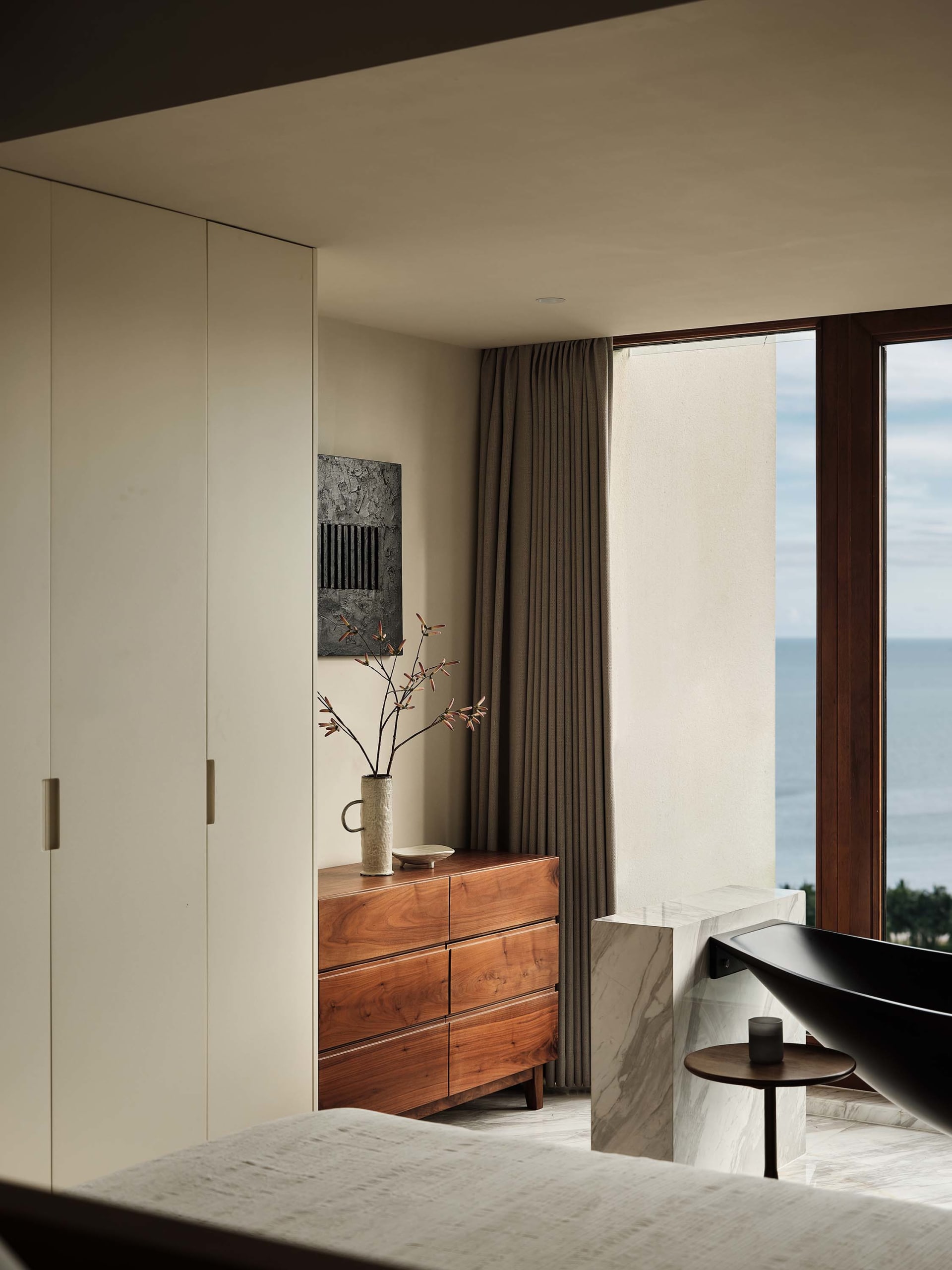 Minimalist bedroom with natural wood furniture and a view of the ocean.