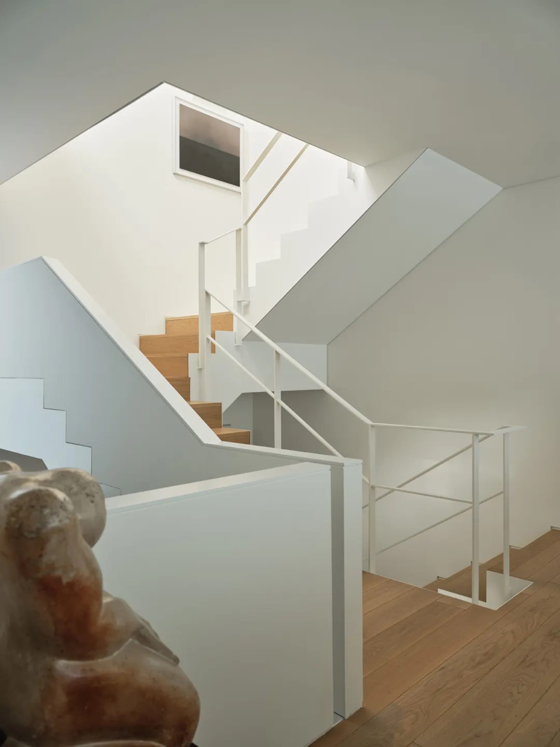 Modern interior design featuring white stairs with wooden steps, white walls, and a minimalist aesthetic.
