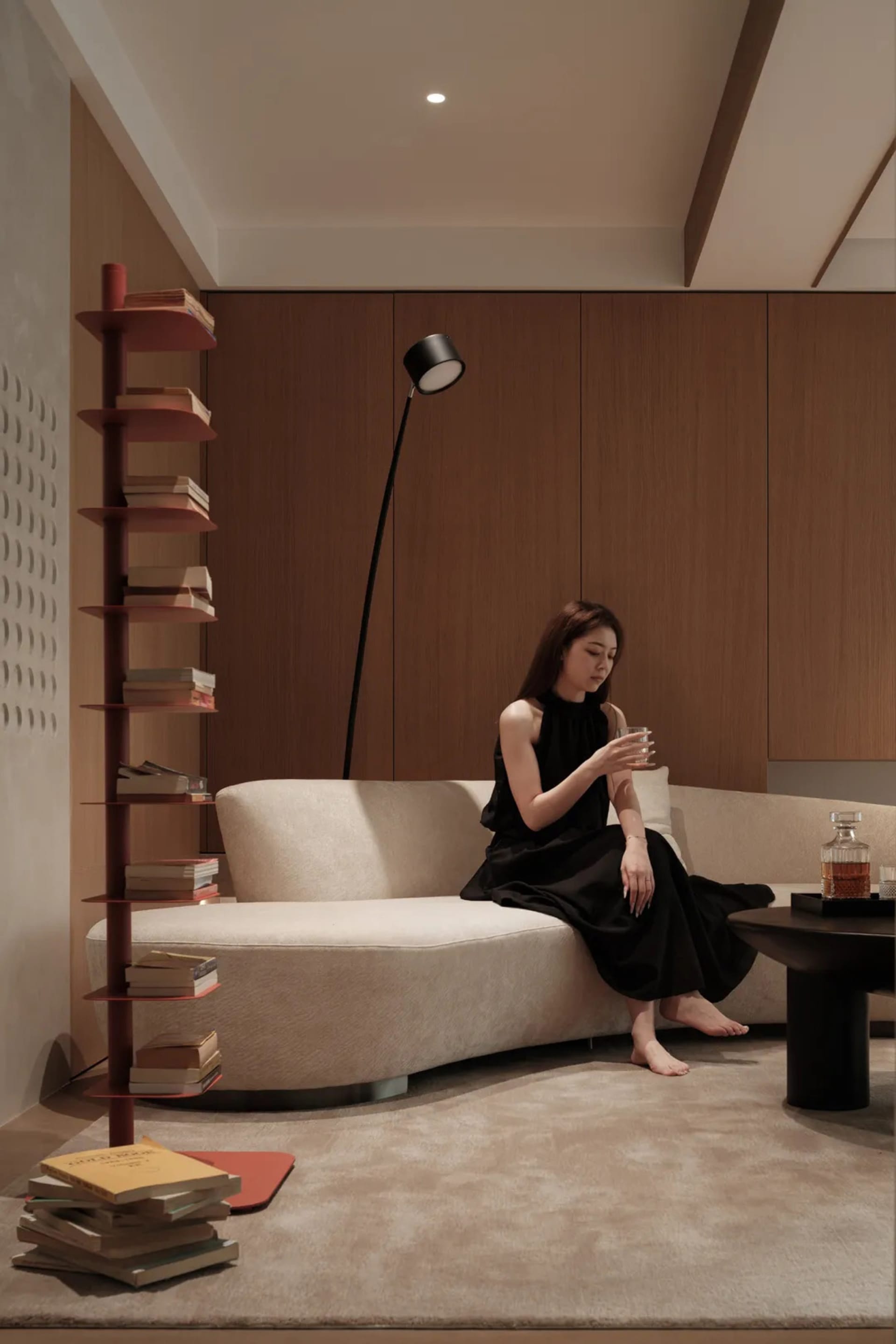 A modern living room featuring a sleek, curved sofa, a tall bookshelf, and a minimalist floor lamp.