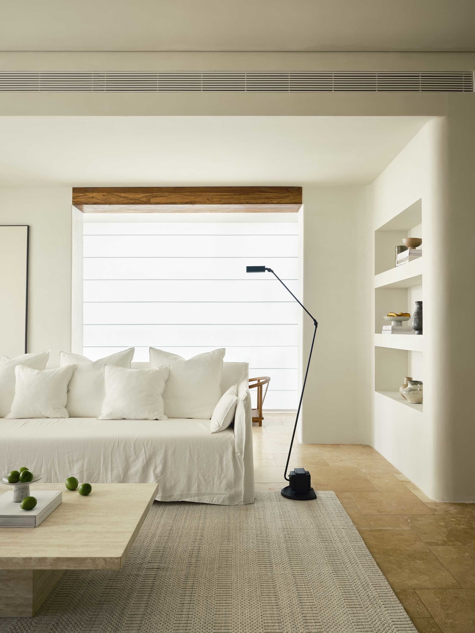 Modern living room featuring a white couch with multiple pillows and a black floor lamp on a beige rug in front of a window w