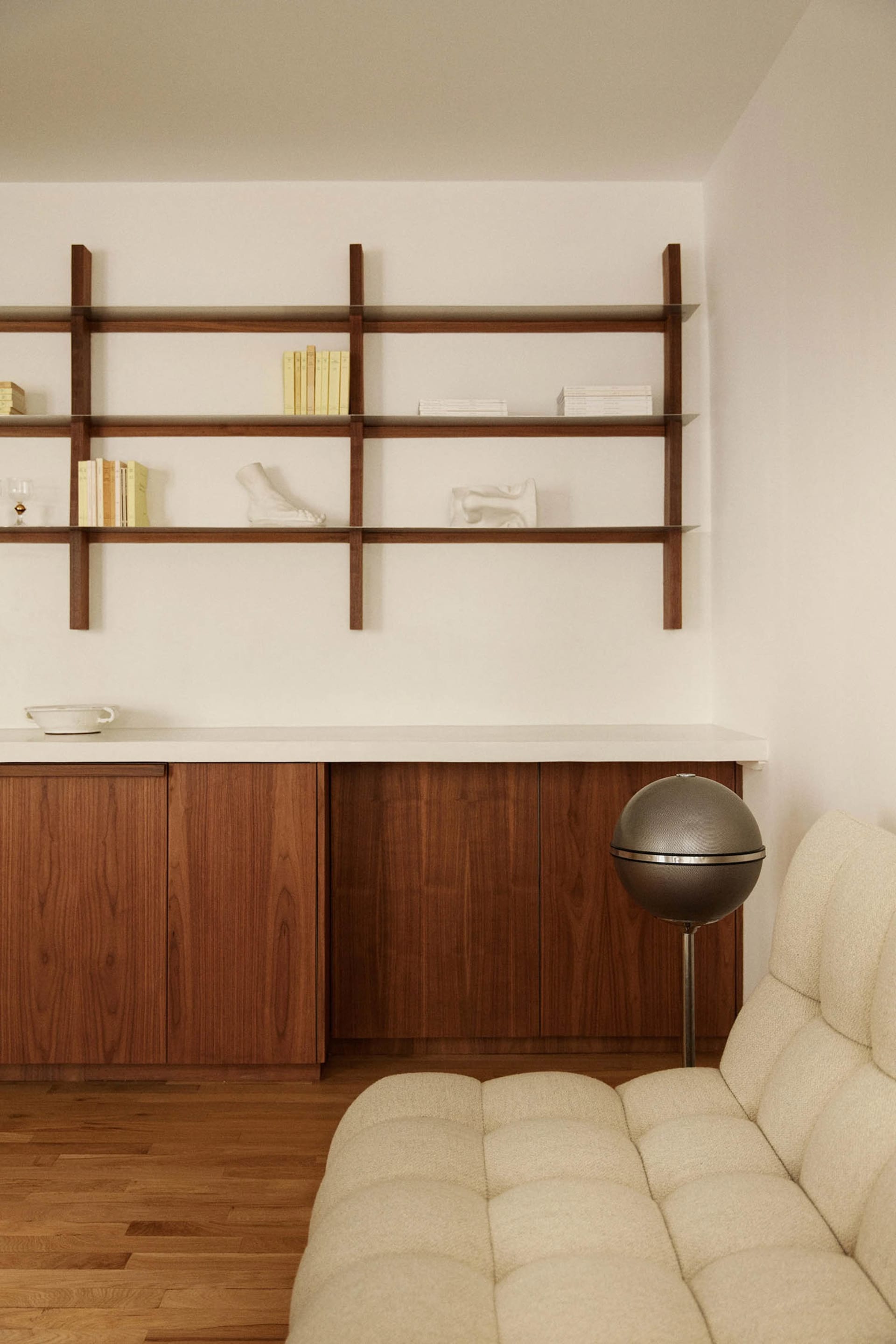 A modern minimalist living room featuring a wooden cabinet, white sofa, and sleek shelving unit.