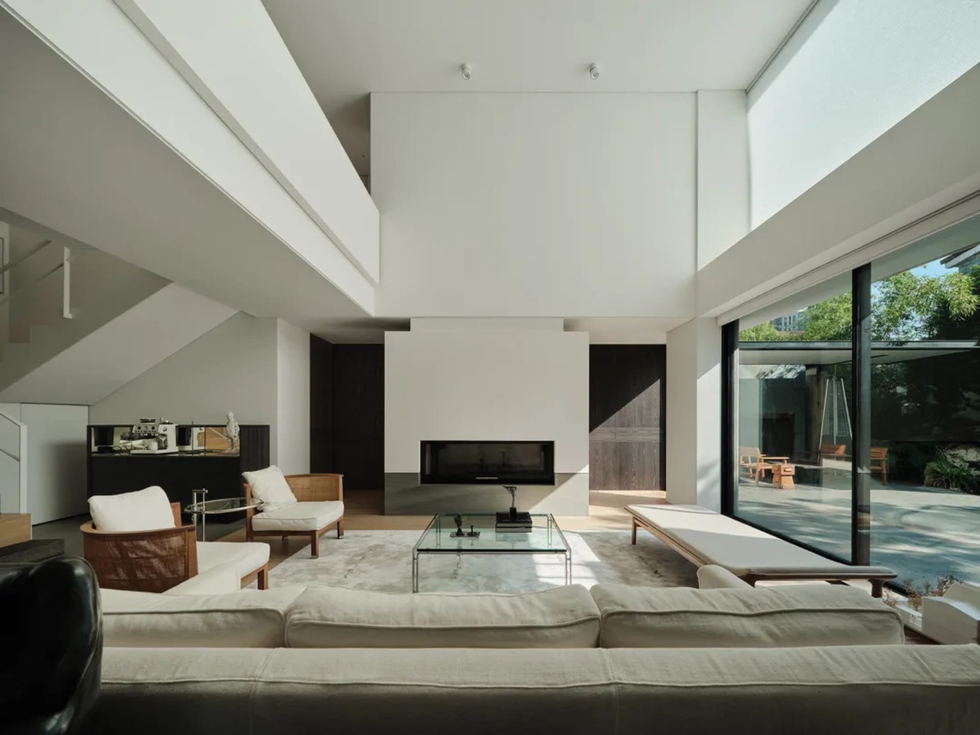 Modern minimalist living room with glass fireplace, white sofa, and wooden accents, featuring a glass coffee table and large