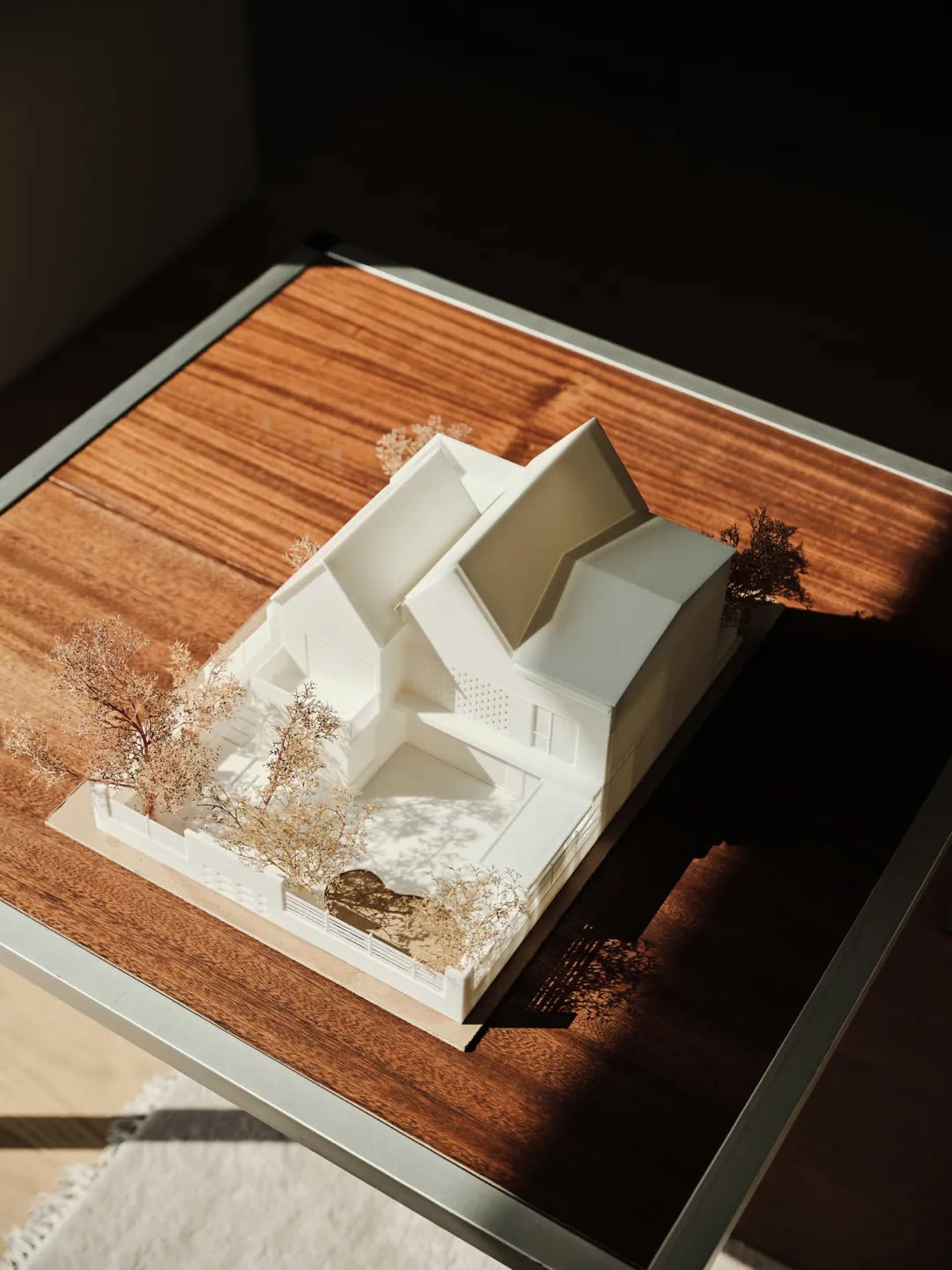 A modern house model made of plastic, featuring a unique architectural design with a central courtyard, surrounded by trees a