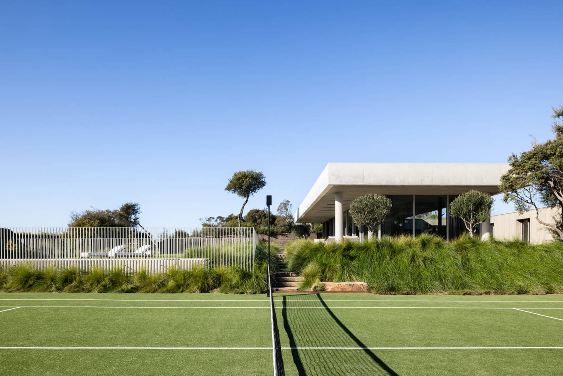 A modern house with a green tennis court and metal fence.