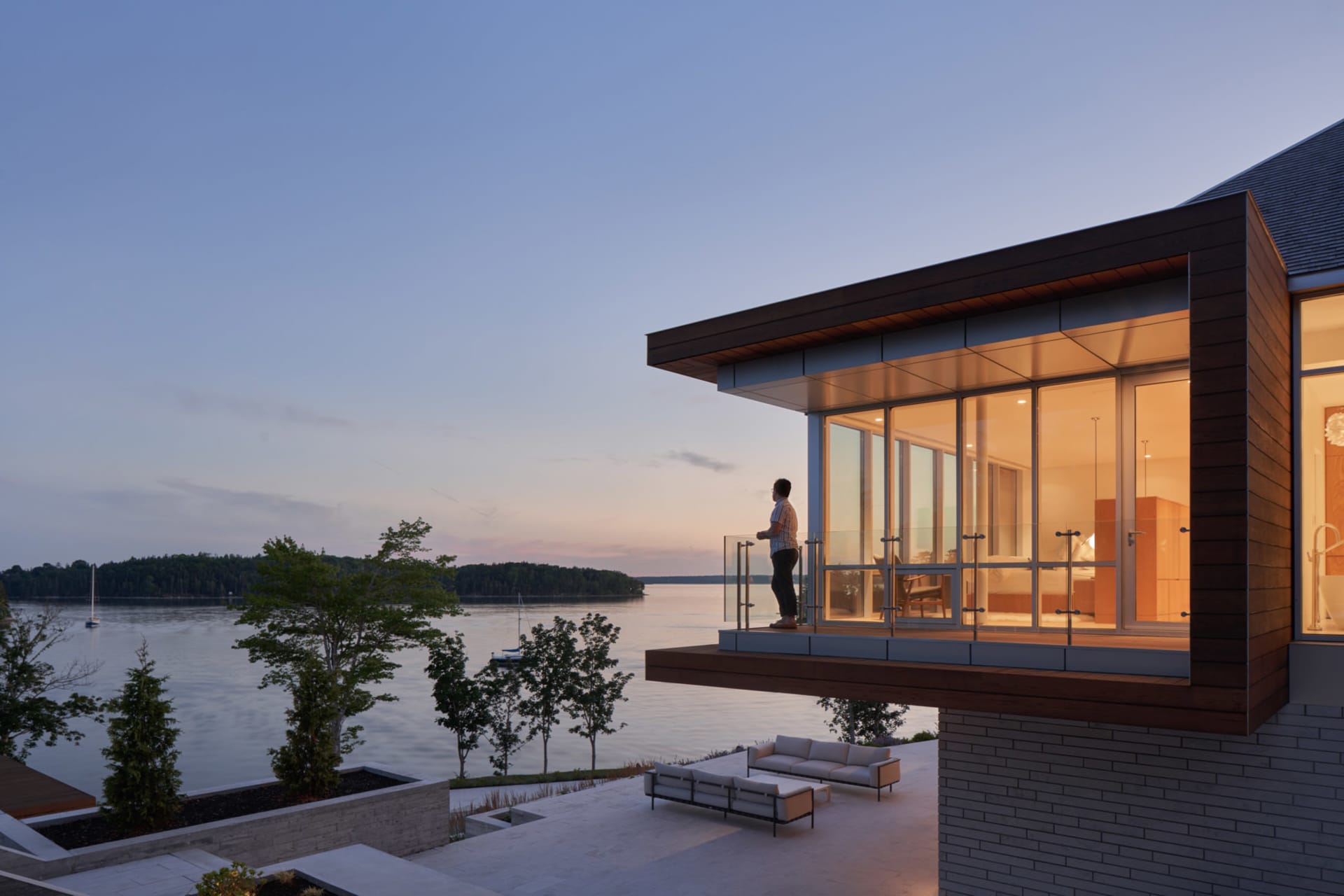 A modern residential patio overlooking a lake, featuring wood, metal, and glass elements.
