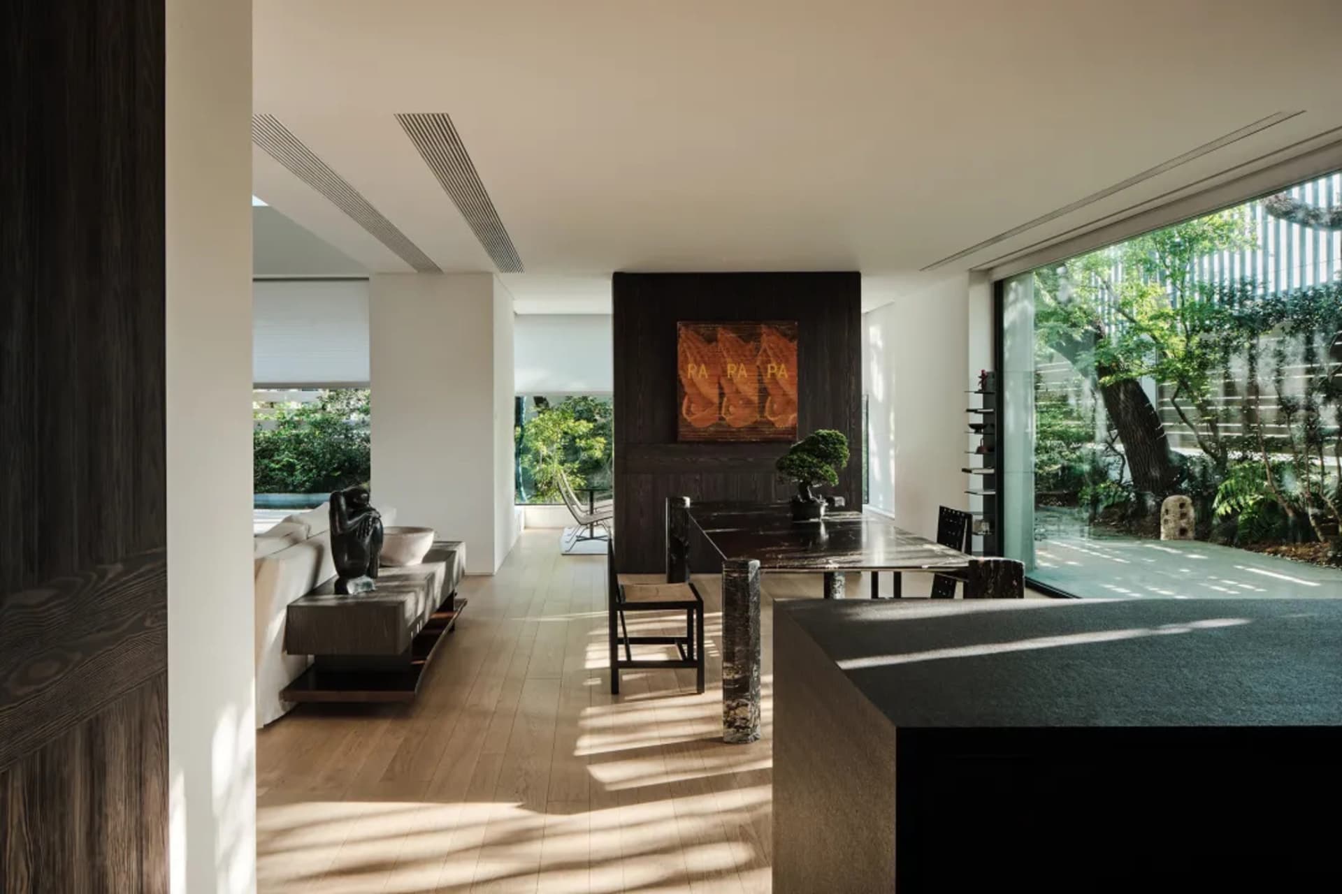 Modern living room with wooden furniture and large windows overlooking greenery.