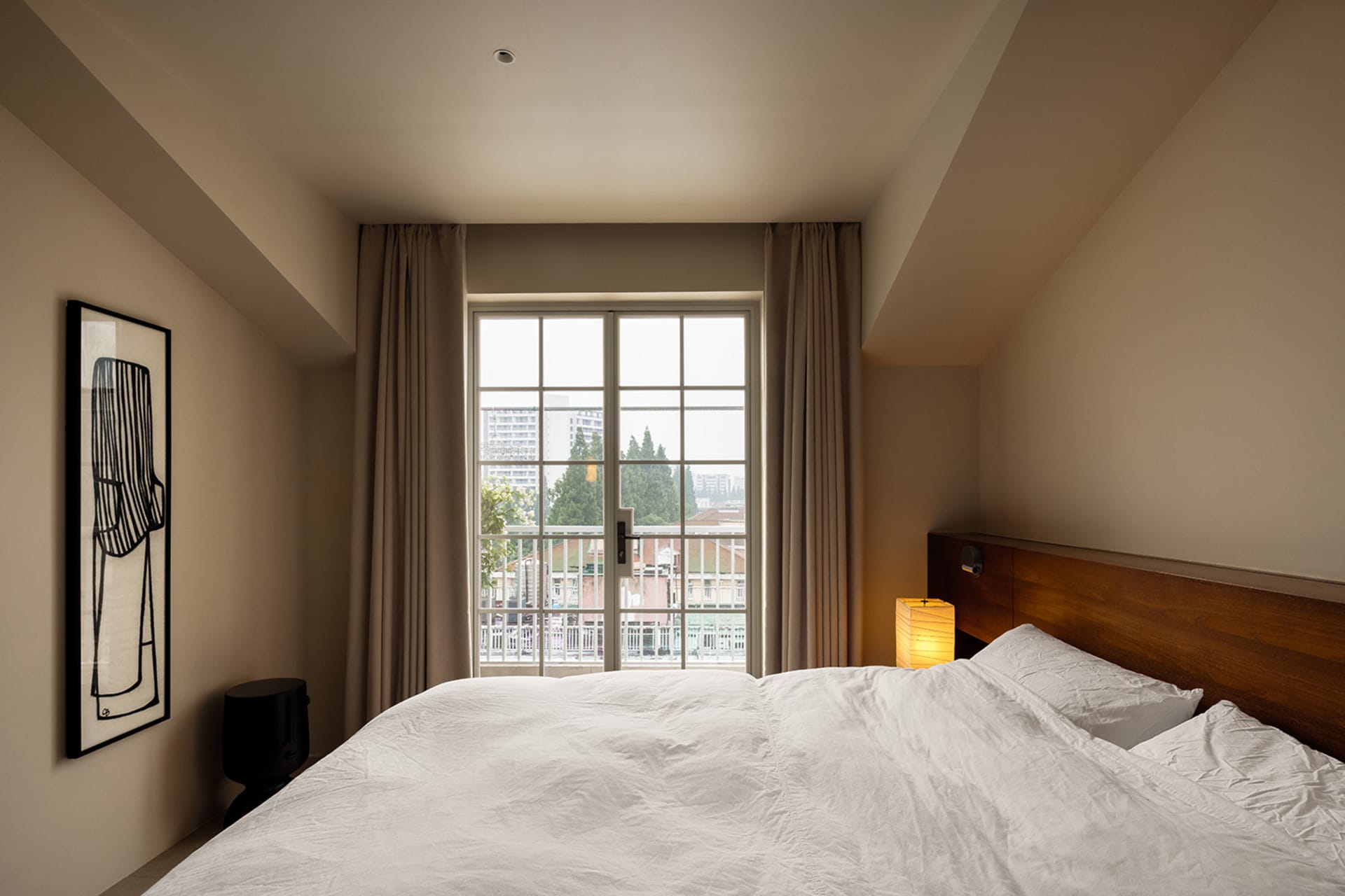 A modern minimalist bedroom with a white fabric bed, wooden headboard, and glass balcony.