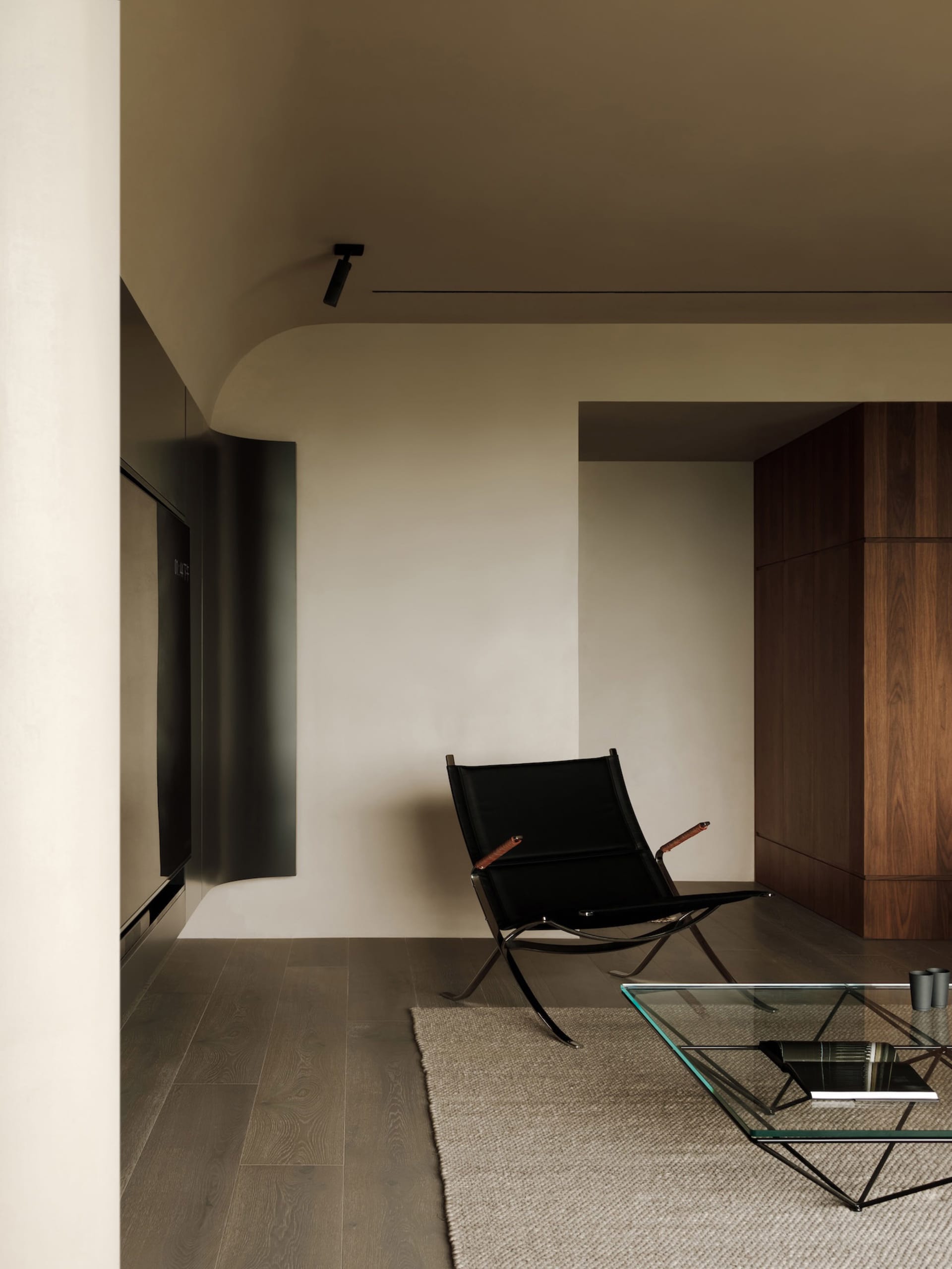 A minimalist living room featuring a black leather chair, wooden flooring, and a sleek coffee table.