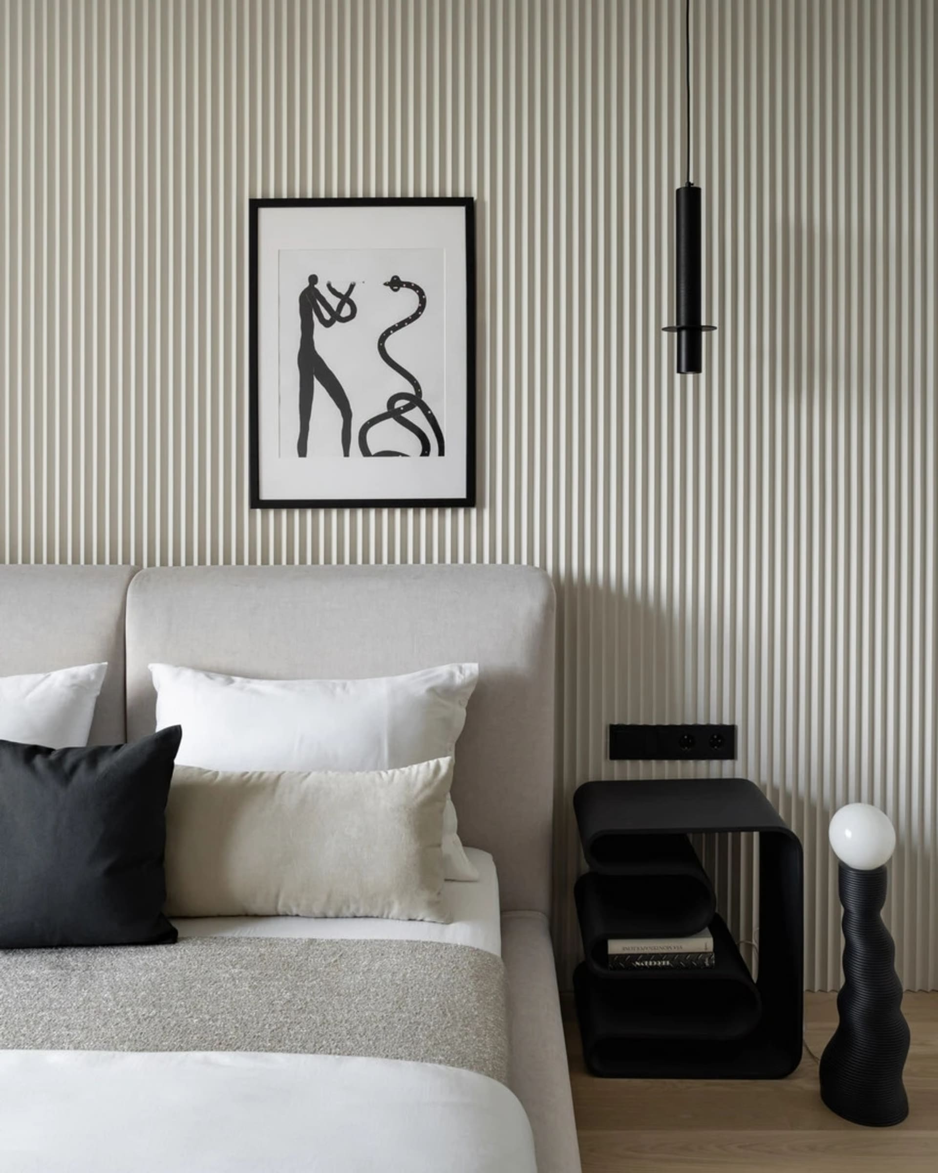 A modern minimalist bedroom with a light-colored upholstered bed, white and black pillows, and a geometric light fixture.
