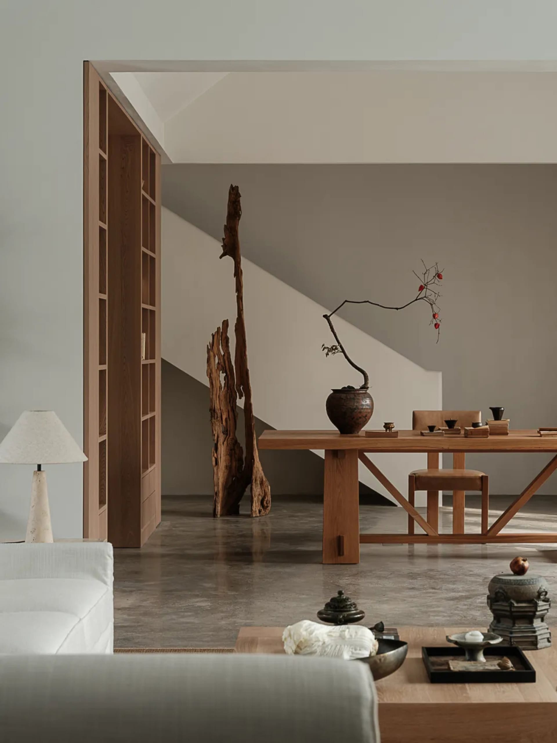 A minimalist living room with a wooden table, chairs, and coffee table, featuring an abstract wooden sculpture as a decorativ