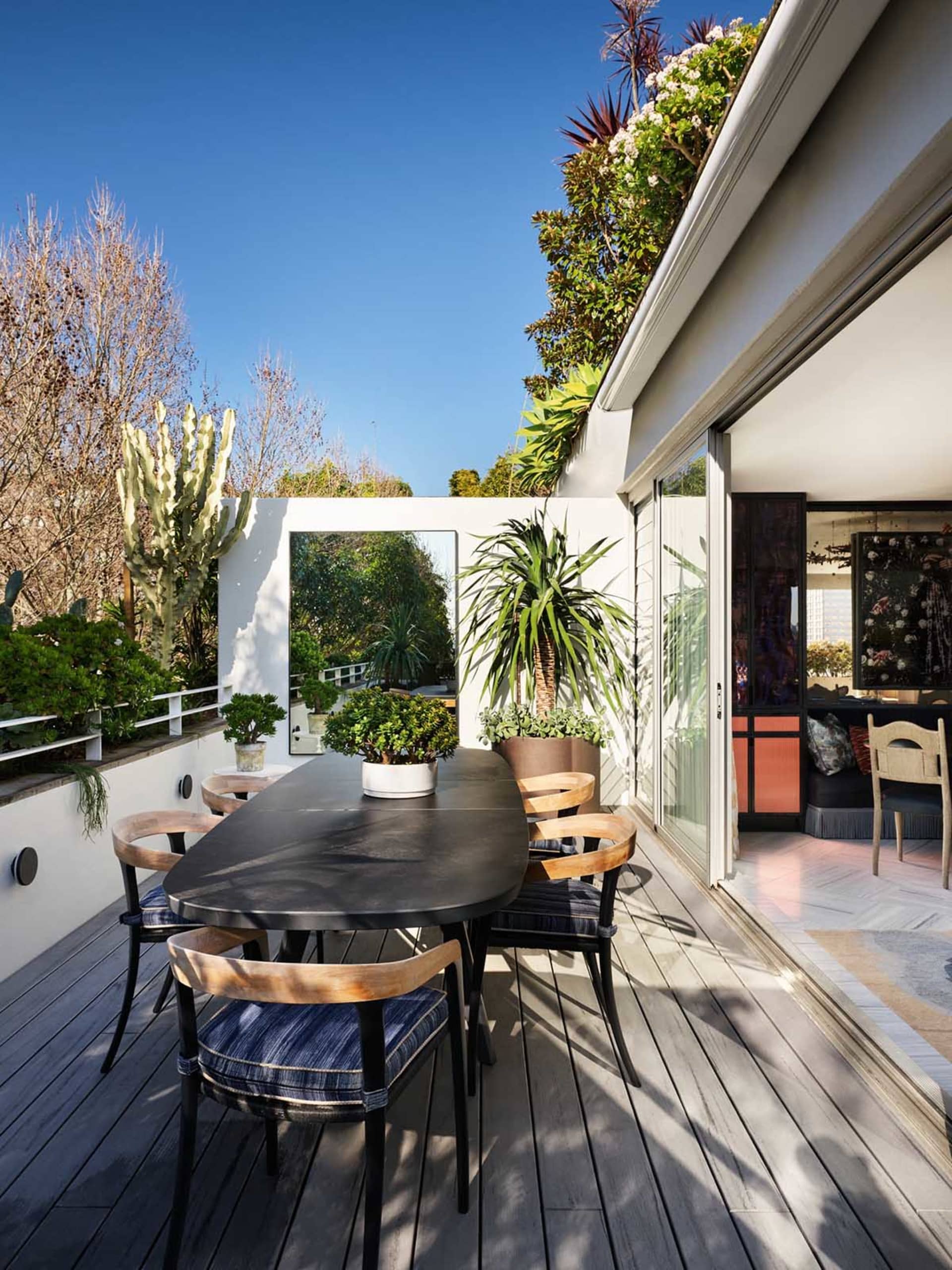 Modern, outdoor office space with a dining table, chairs, and potted plants under blue sky.