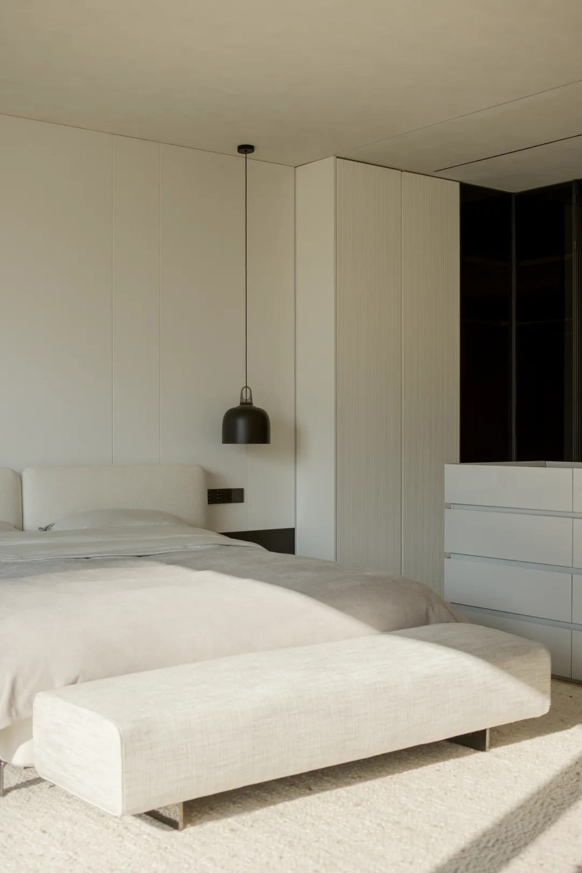 A minimalist bedroom with white furniture and a large window.