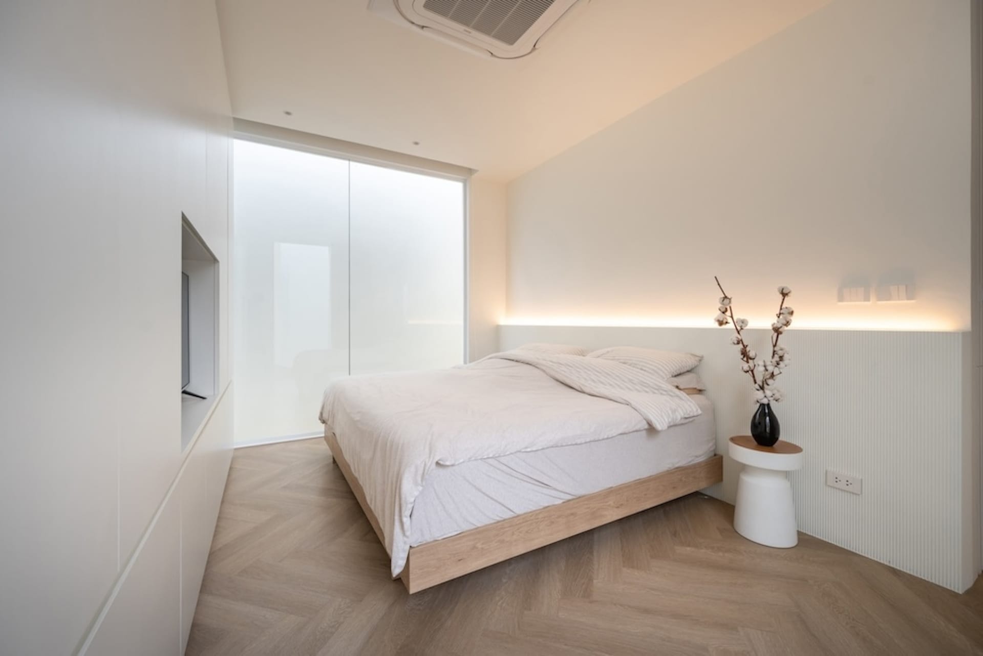 Minimalist bedroom with white bedding, wood floor, and frosted glass wall.