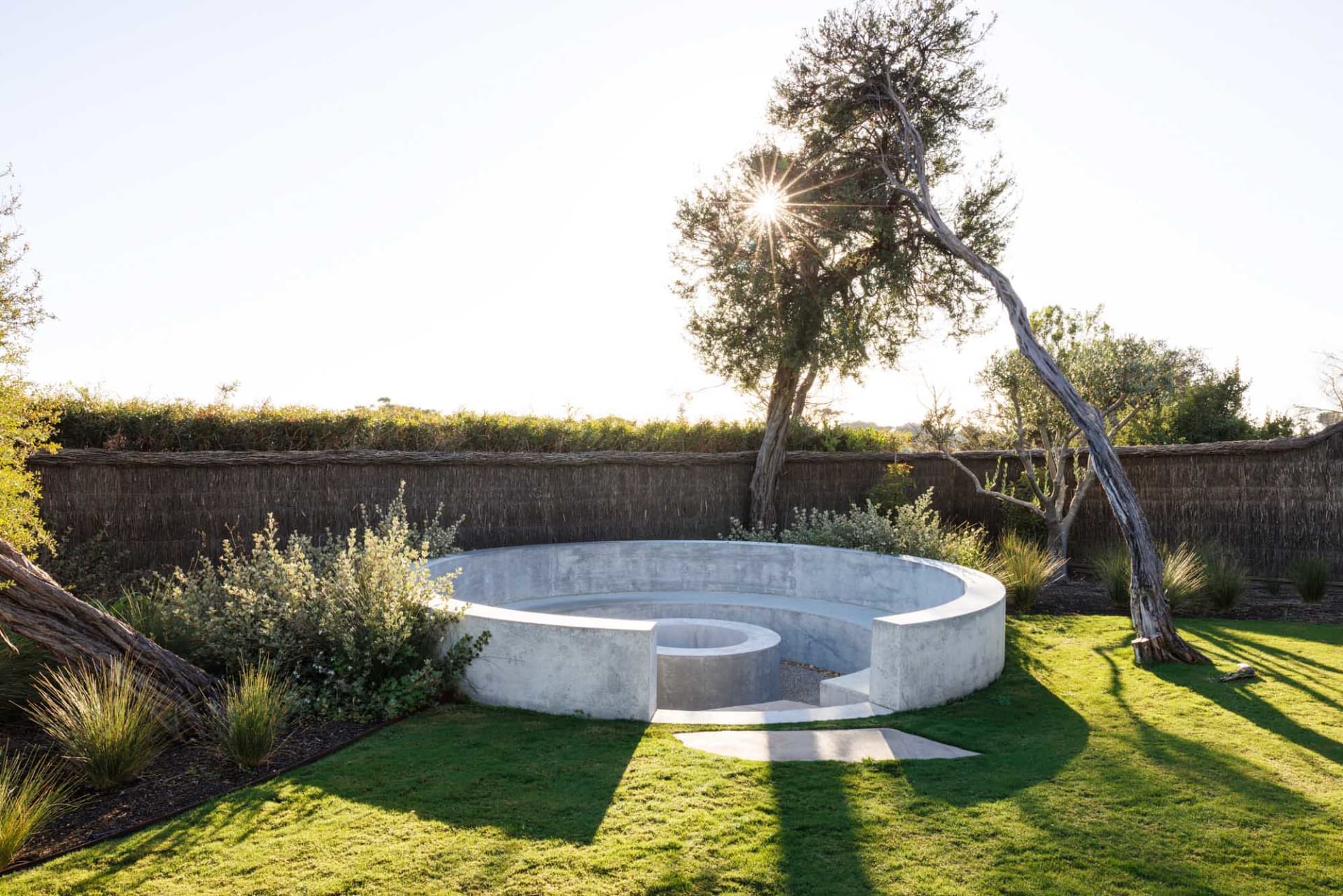 Circular concrete seating area in a modern garden with lush greenery and a sunlit sky.