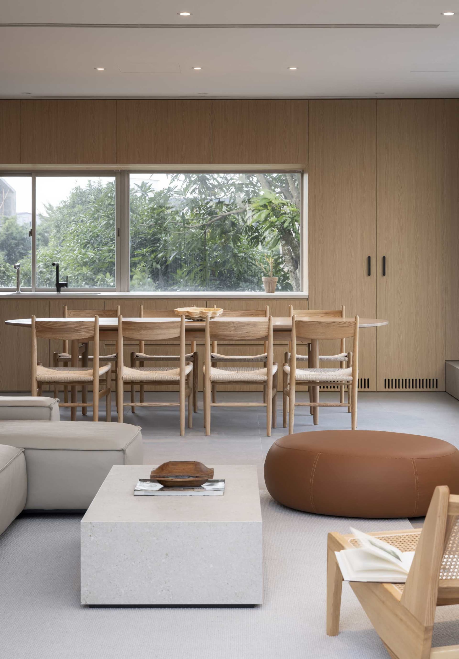 A modern living and dining space featuring wooden furniture and concrete floors, with a large window overlooking greenery.
