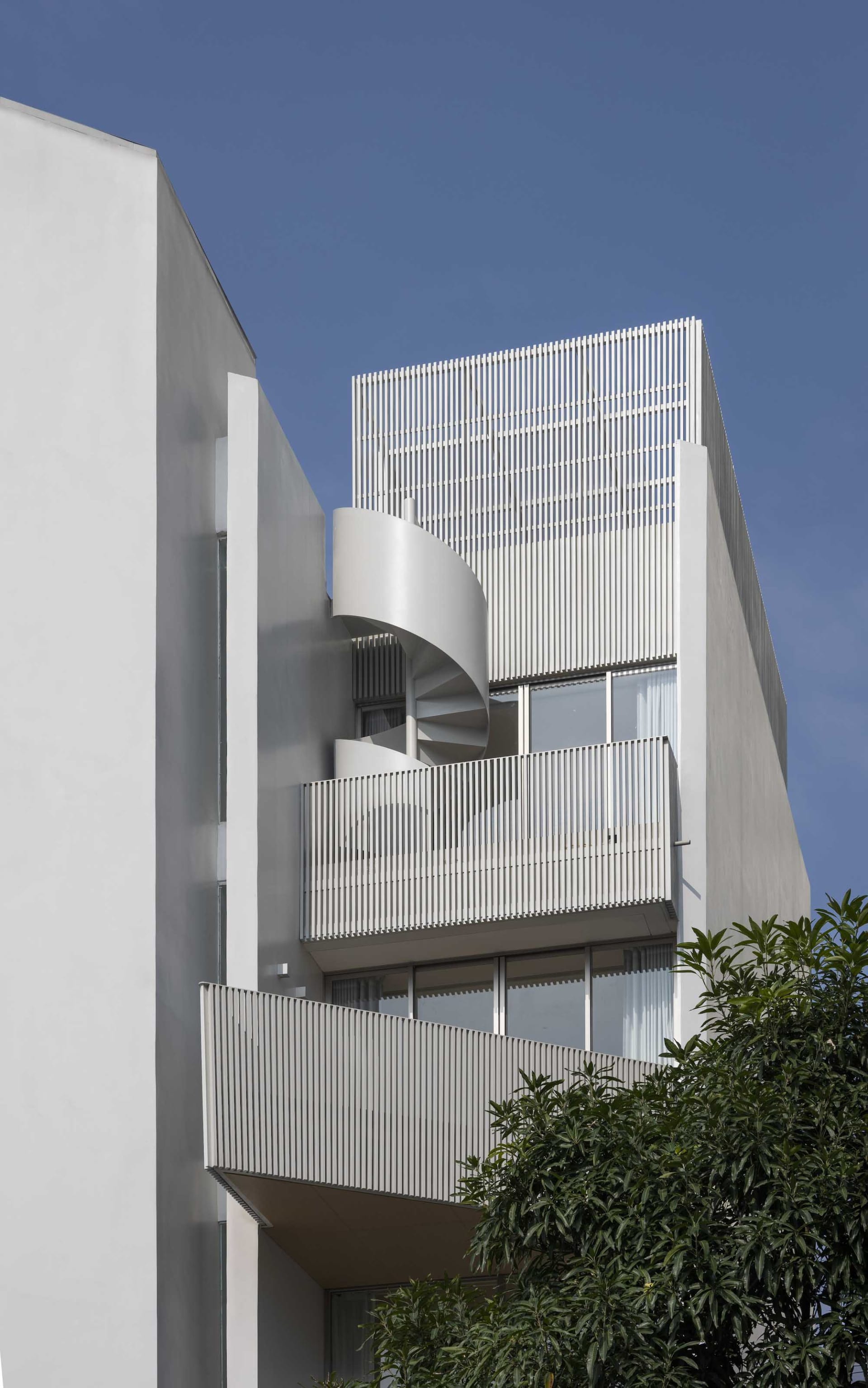 Modern minimalist residential building with aluminum panels and a spiral staircase.