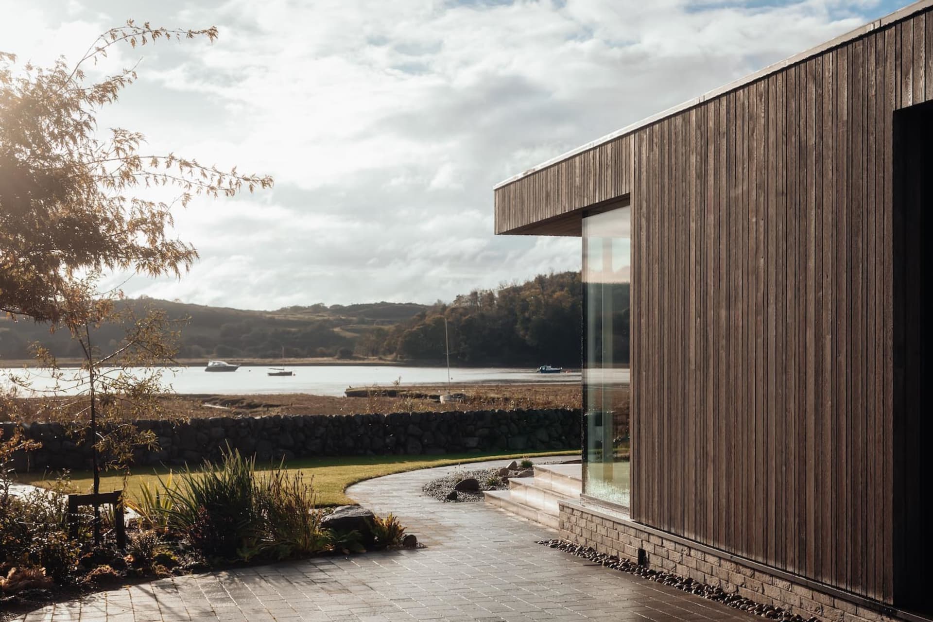 Modern residential exterior featuring wooden panels and glass windows overlooking a scenic lakeside view.