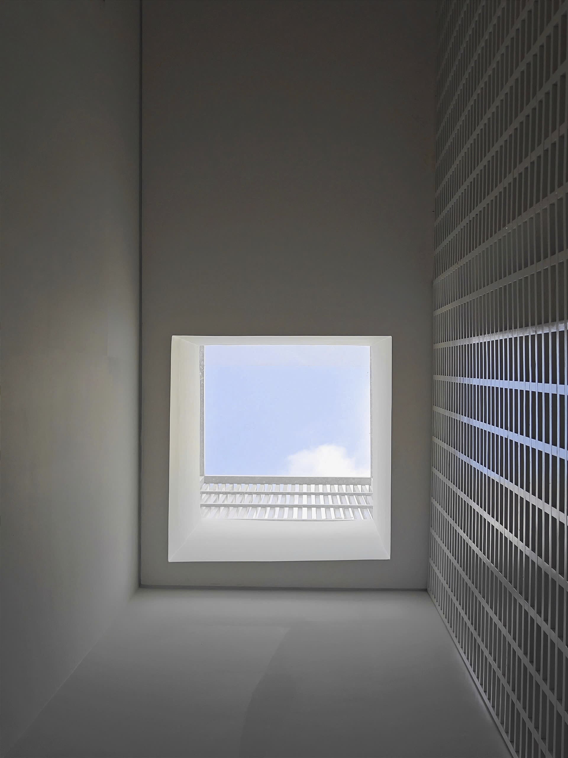 A minimalist, metallic window frame with a steel panel design, set in a white, industrial-style room with a grid-like wall pa