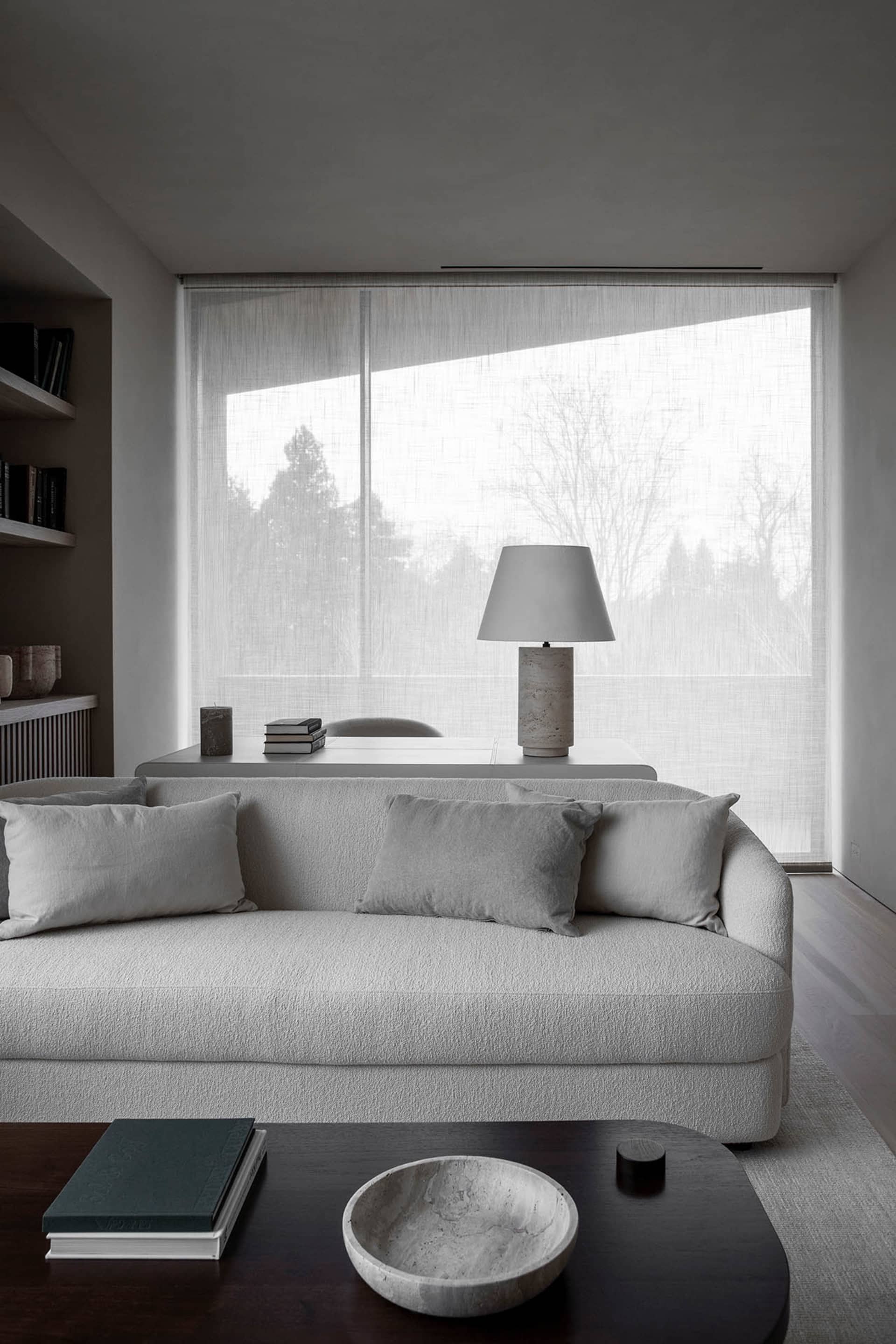 Minimalist living room with a neutral-toned sofa, coffee table, and a large window allowing natural light to fill the space.
