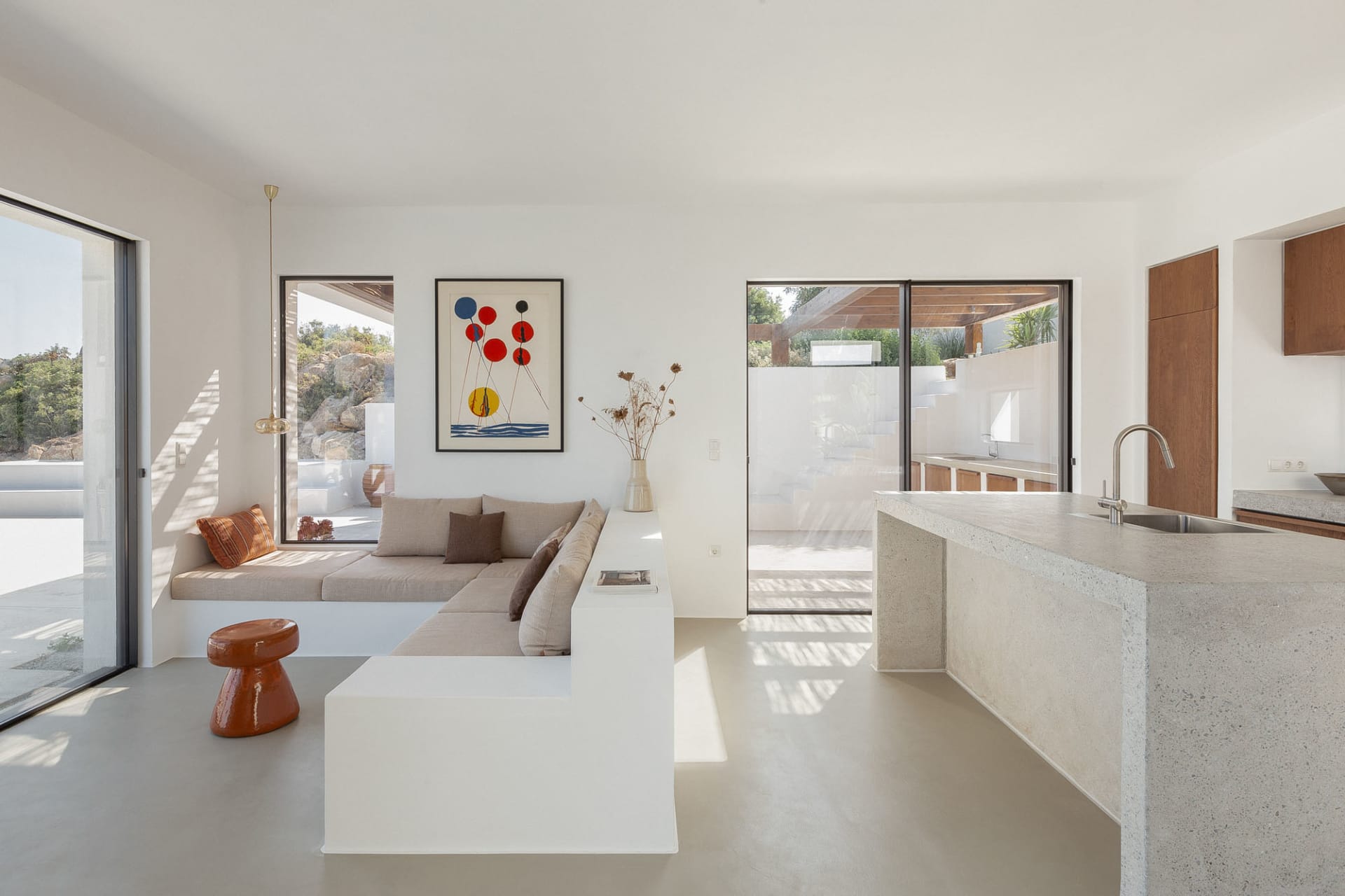 A modern living room with concrete flooring, minimalist furniture, and abstract art on the wall, featuring a built-in bench s