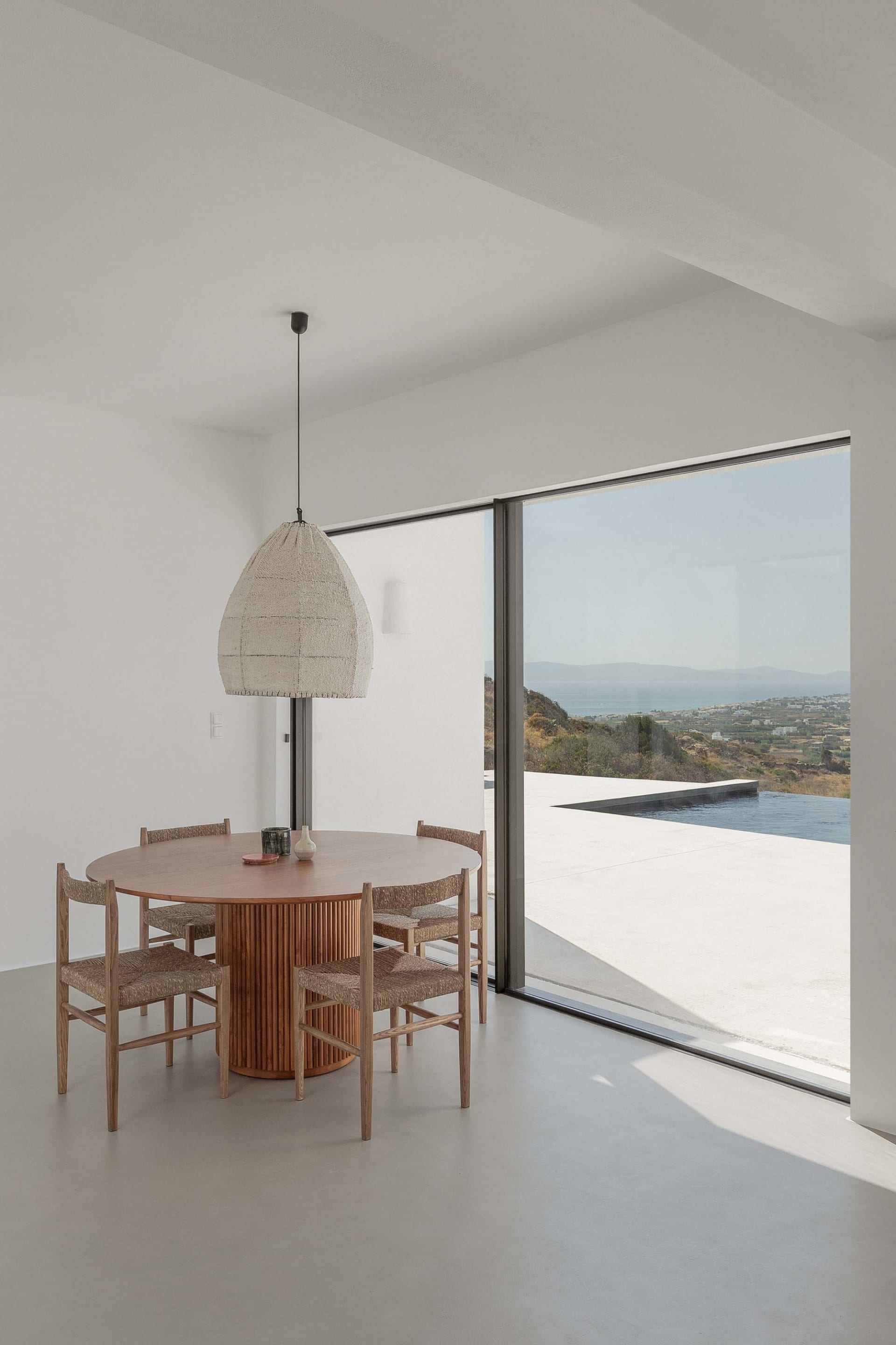 Modern dining room with a wooden table, concrete columns, and white pendant lighting.