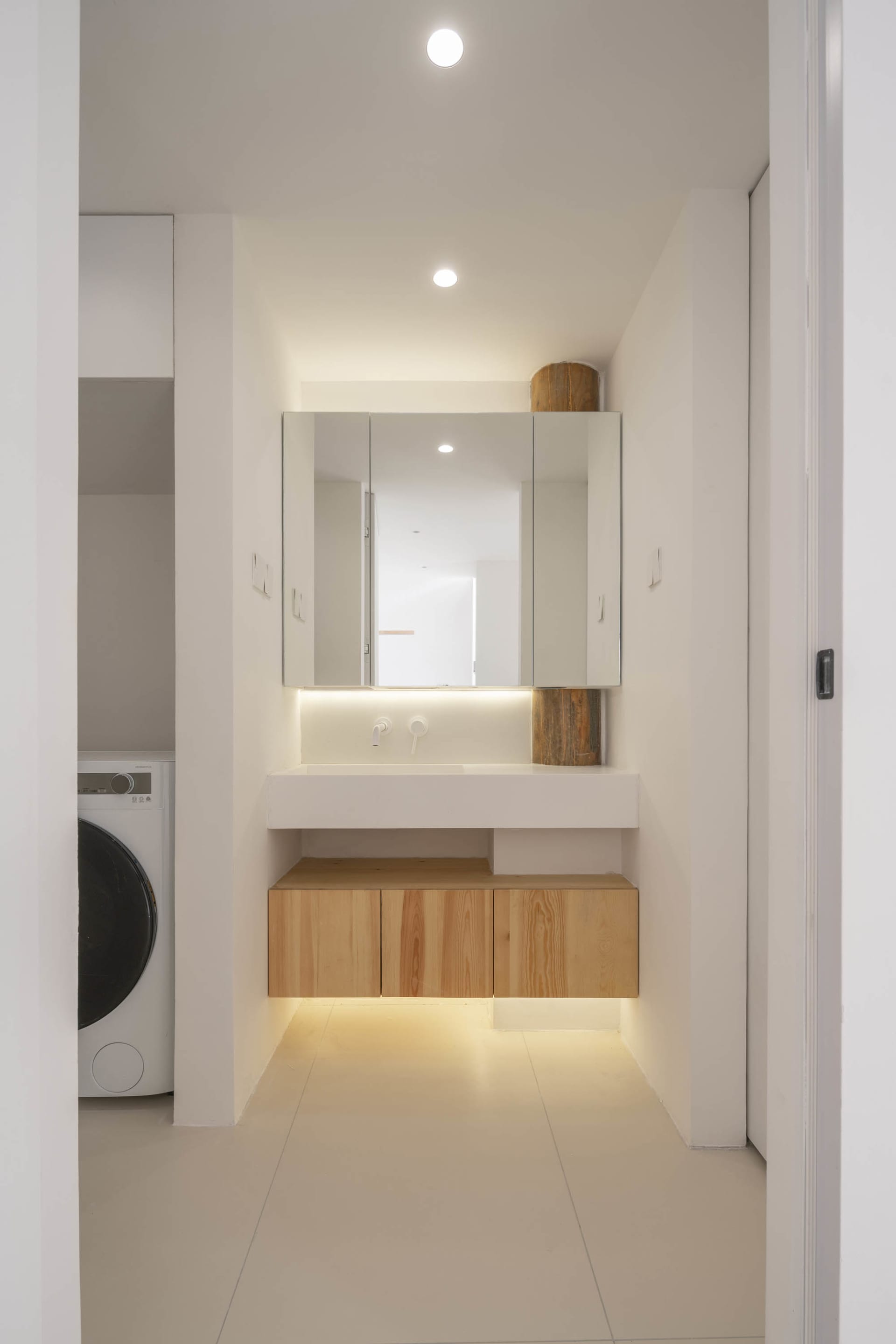 A minimalist bathroom featuring white concrete walls, glass fixtures, and wooden cabinets.