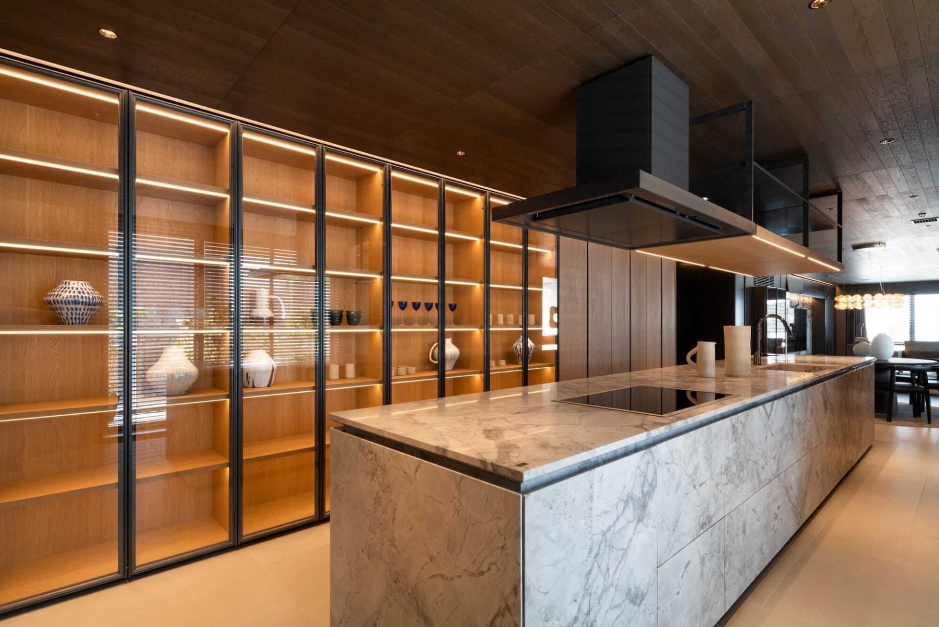 A modern kitchen with marble countertops and illuminated wooden shelving.