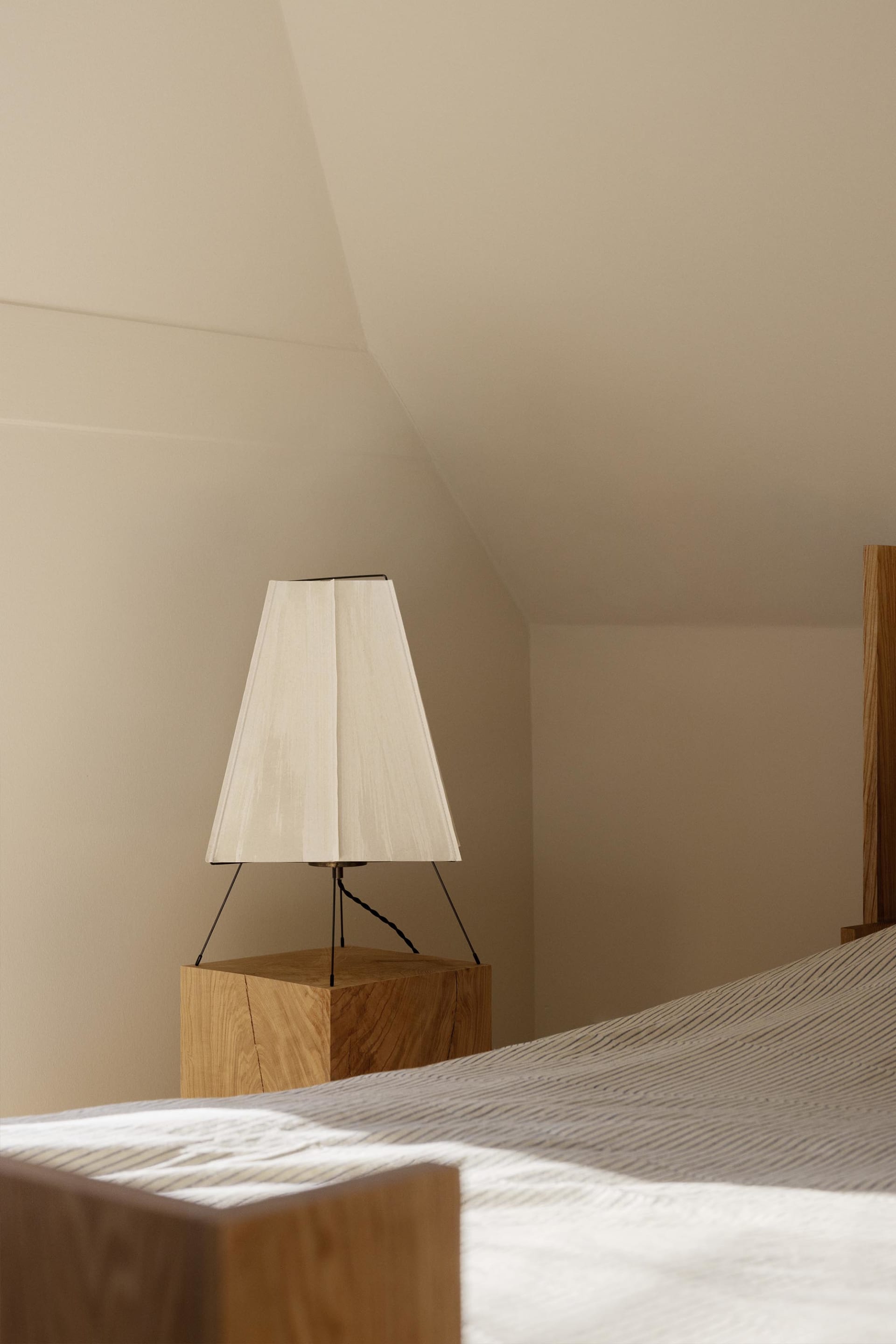 A minimalist bedroom featuring a wooden base lamp with a simple white fabric shade, creating a cozy and contemporary atmosphe