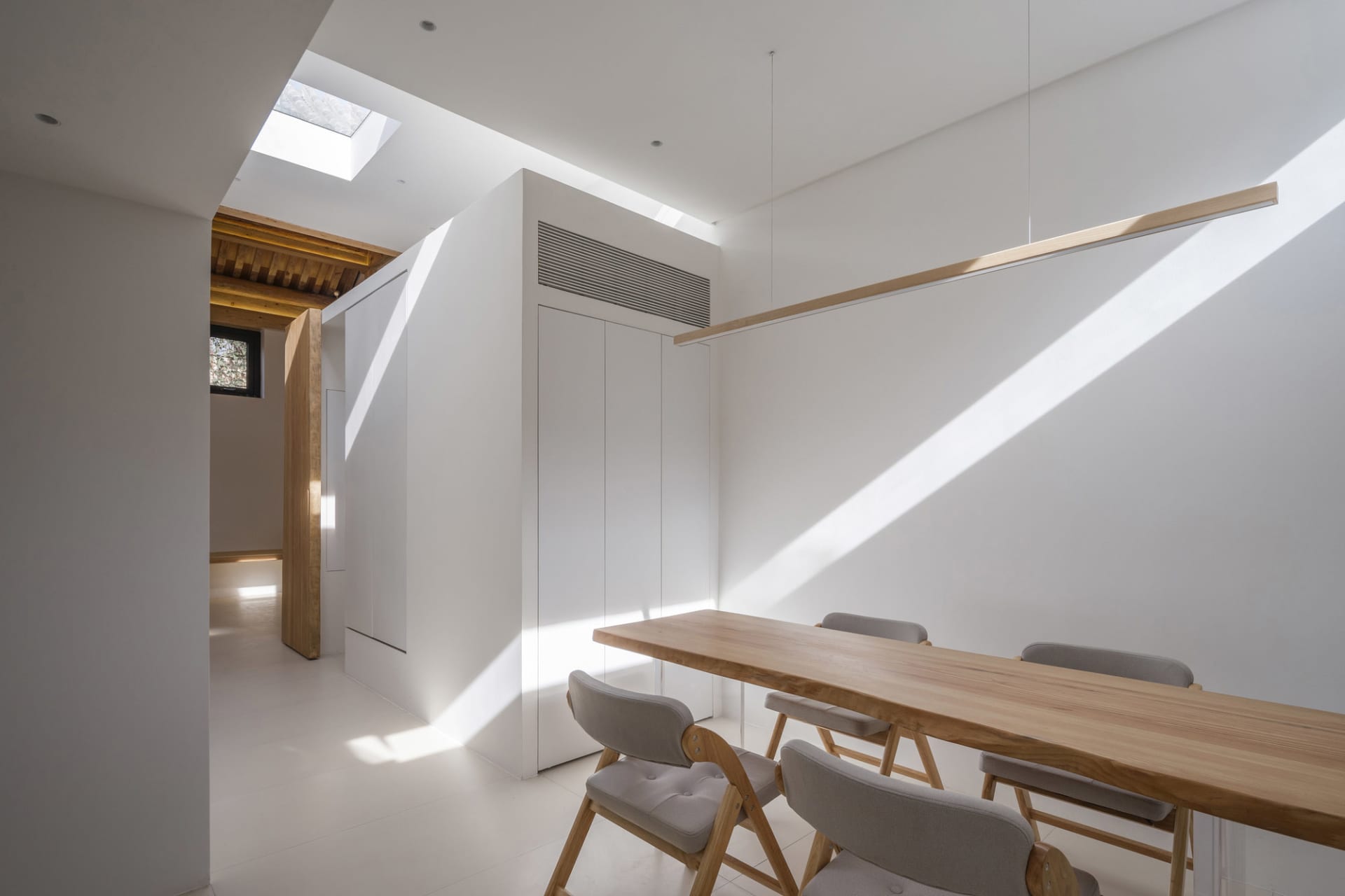 Modern minimalist dining room featuring wooden furniture and white walls.