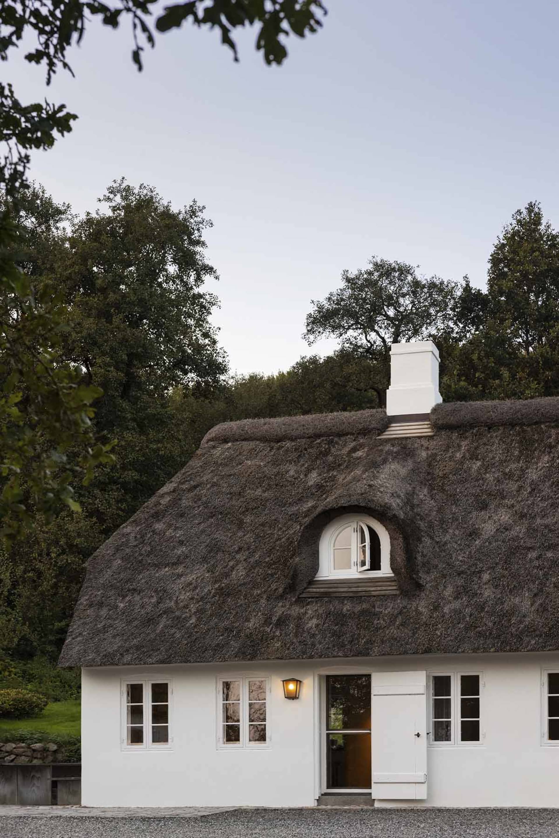 White thatched cottage with a chimney and arched window.