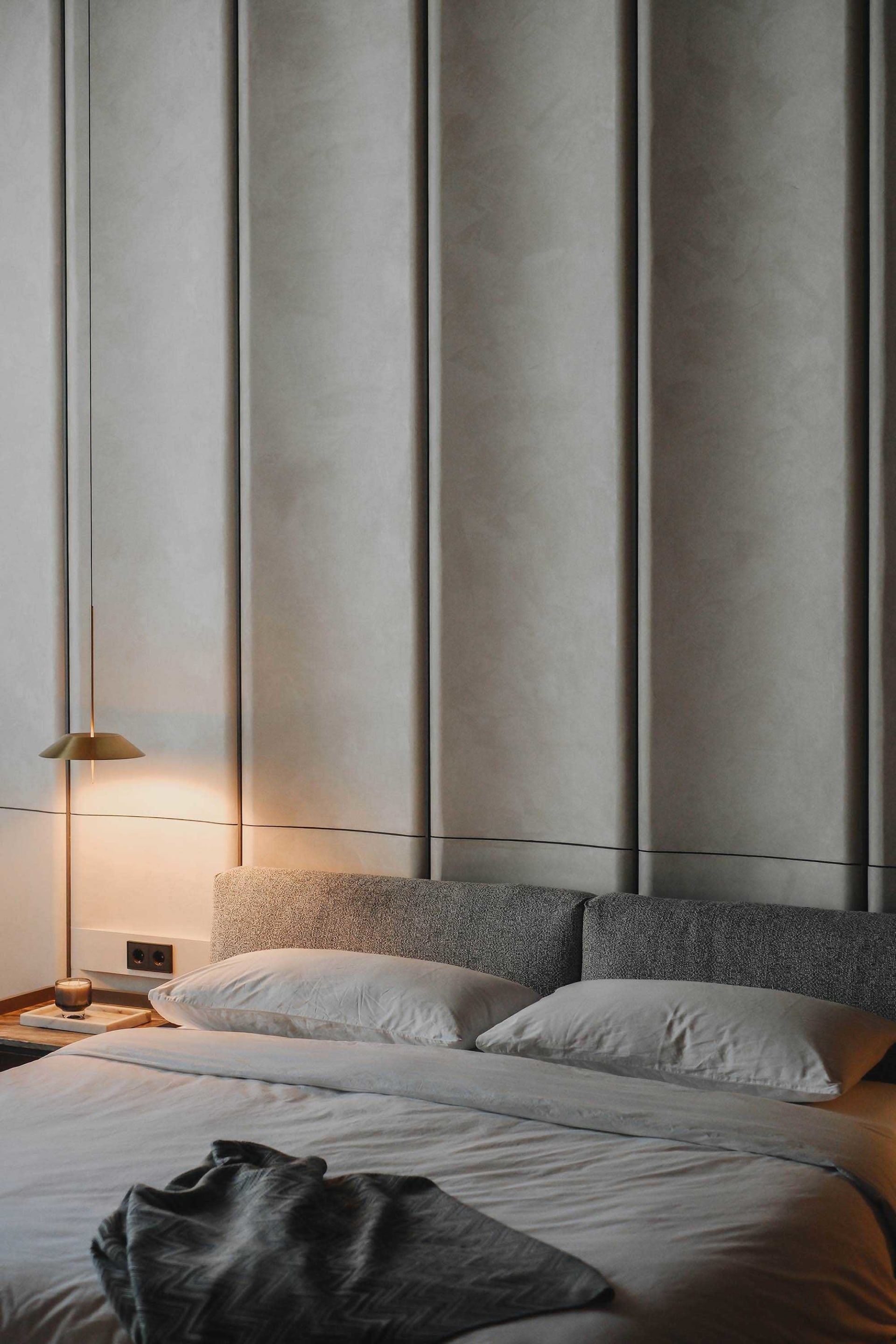 Modern bedroom featuring grey fabric bedding and a grey upholstered headboard against a neutral wall.