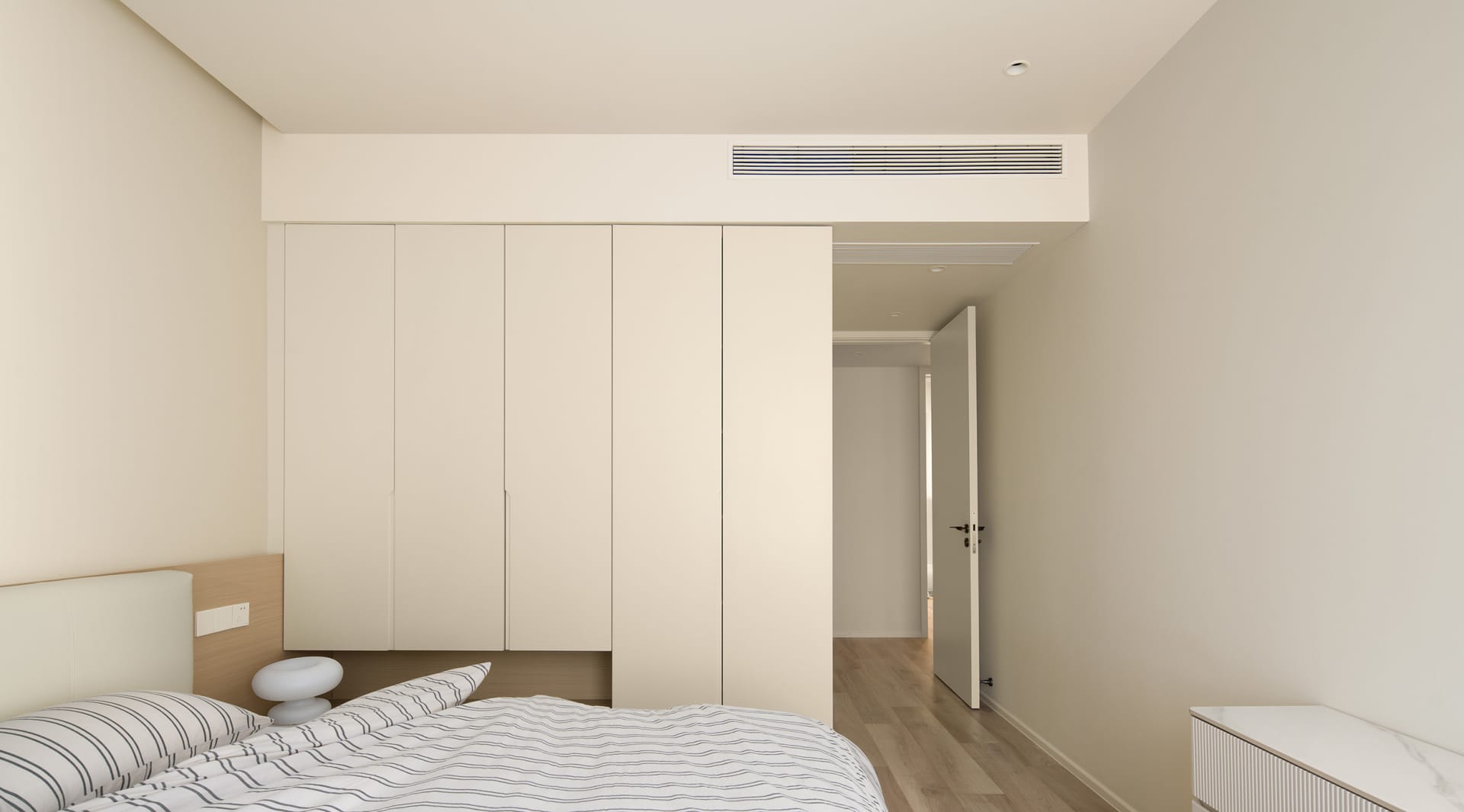 A minimalist bedroom with a white bed, striped bedding, and a white cabinet.