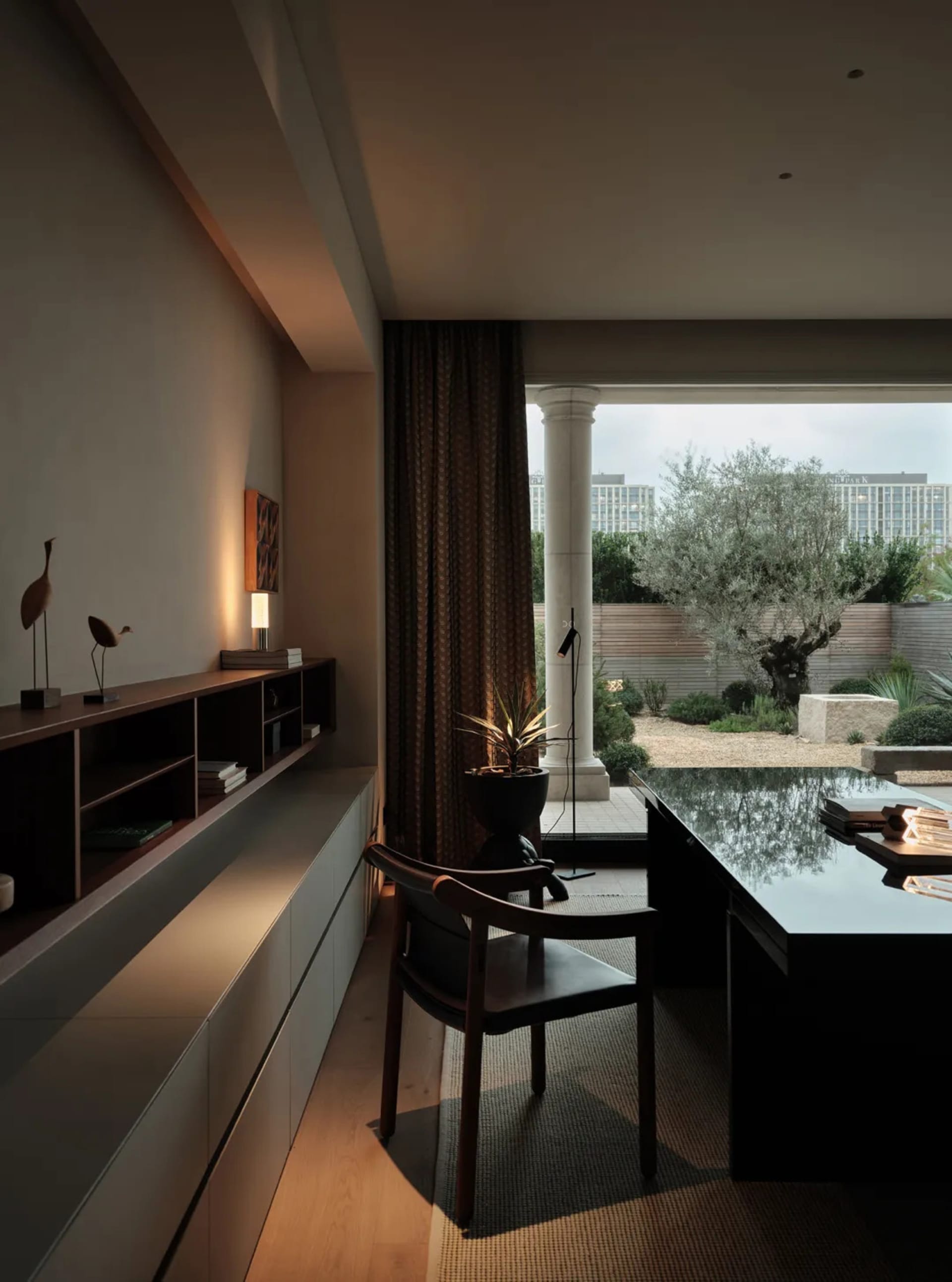 A minimalist living room with wood furniture, featuring a low-profile table, modern lighting, and a large window with curtain