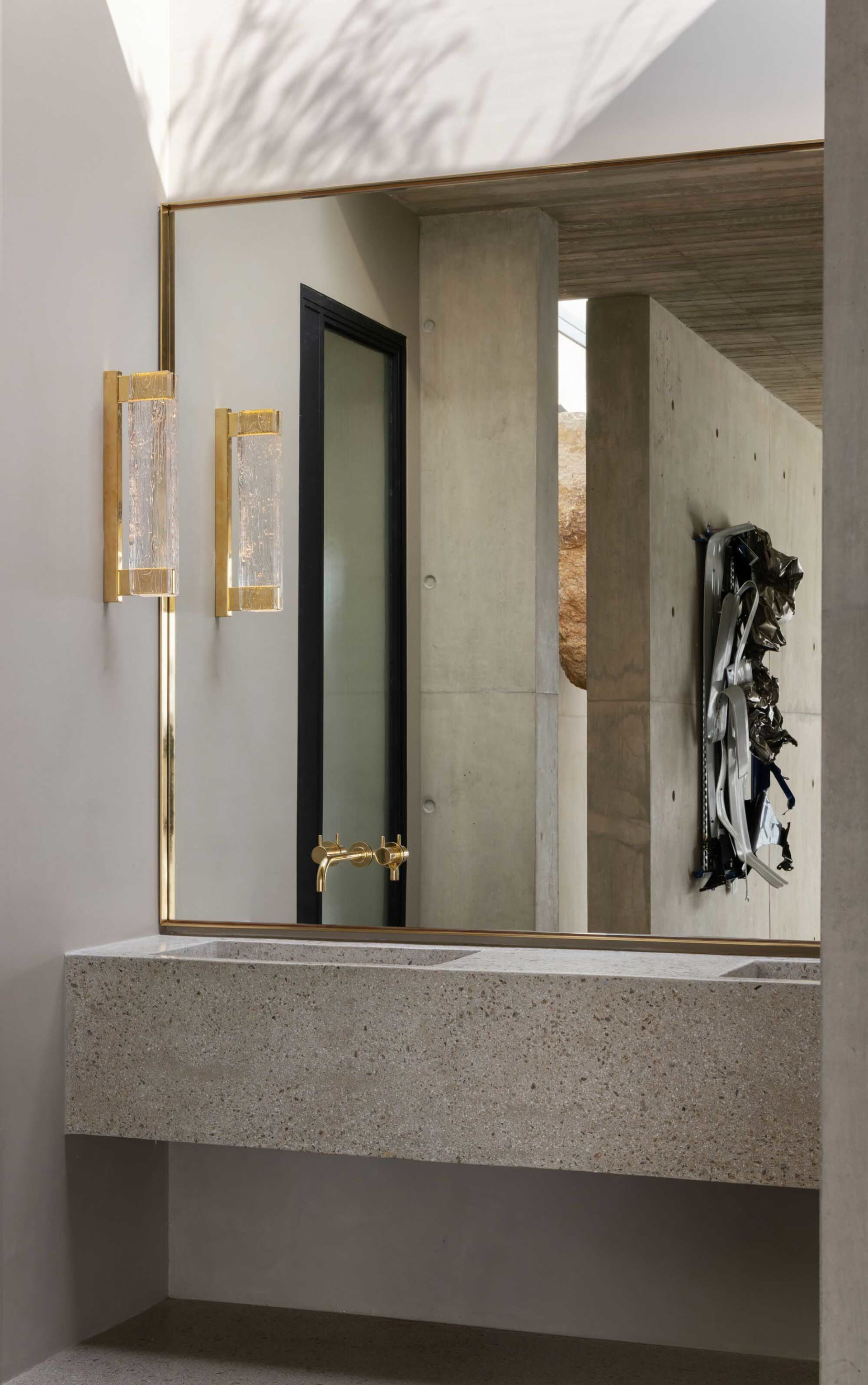 Modern bathroom with concrete vanity, brass faucet, and wall-mounted light fixtures.