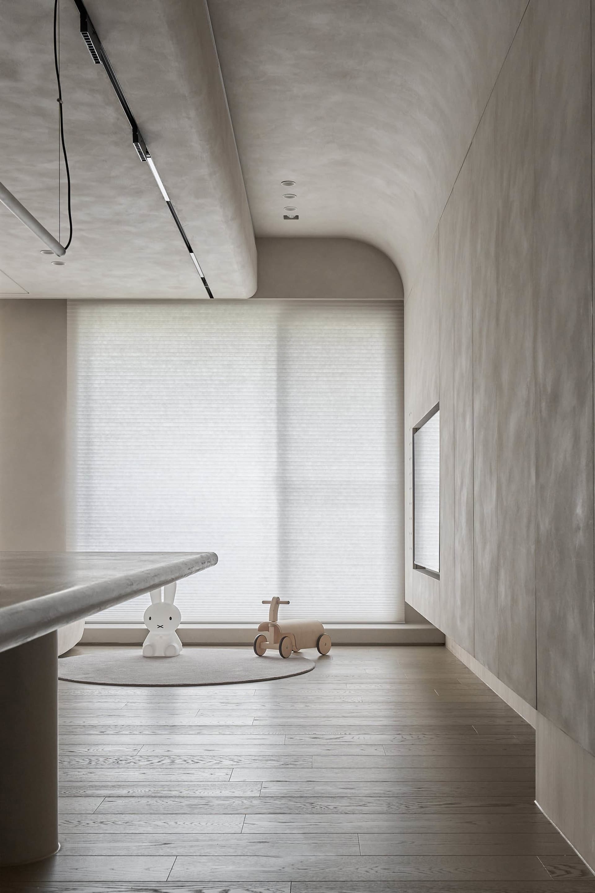 A minimalist living room with concrete walls, wooden floor, and white furniture.