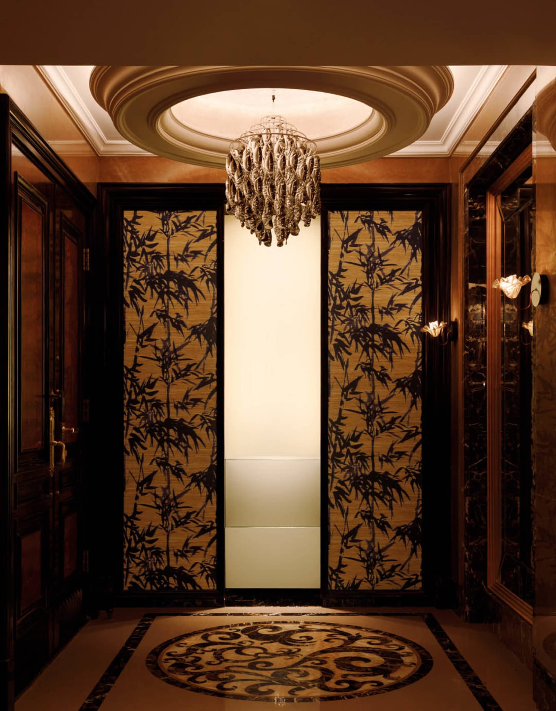 A luxurious entrance area featuring elegant elevators enclosed in glass and framed by rich, wooden elements.